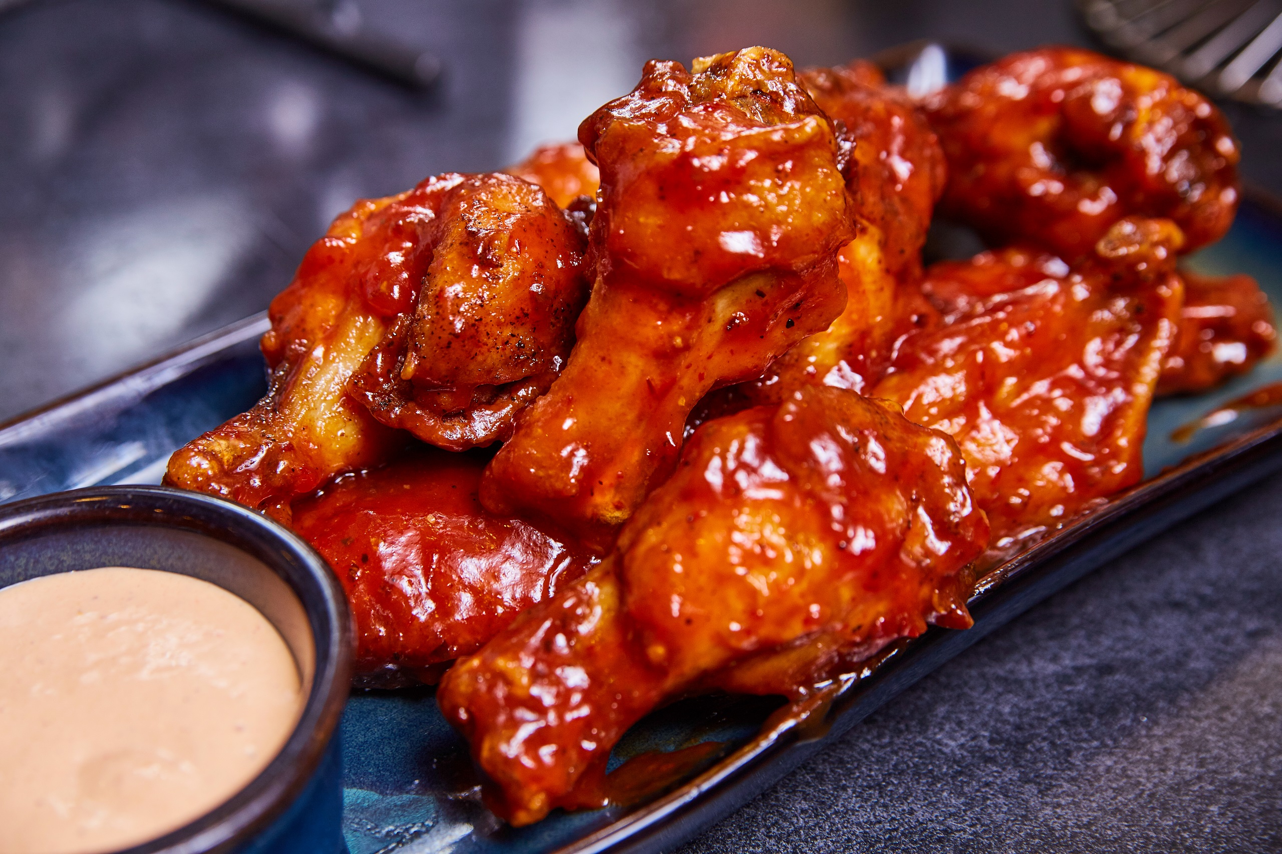 Baked sticky chicken wings served with dipping sauce on a modern blue plate, in a stylish setting.