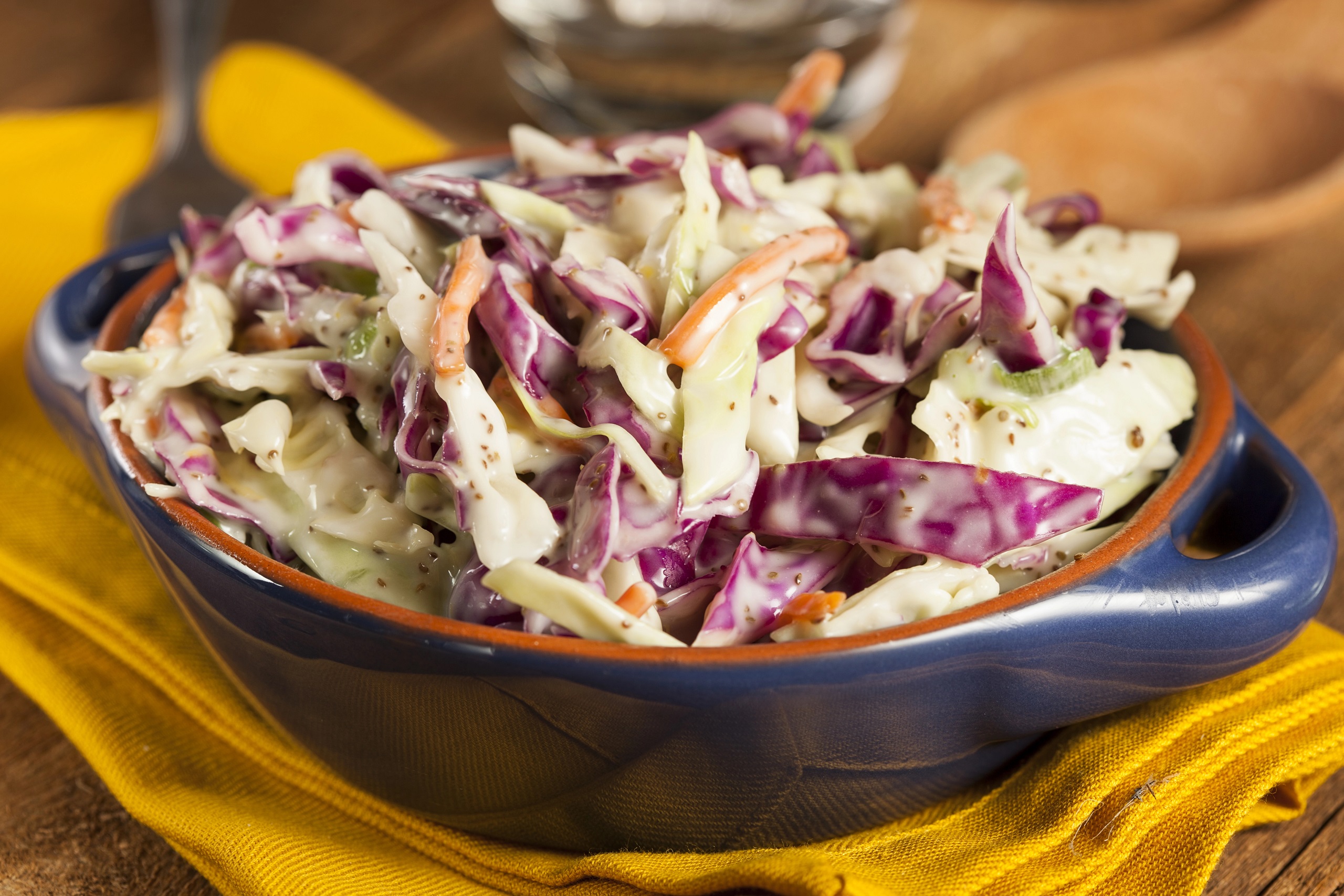 Coleslaw with red cabbage, carrots, and light mayo in a black salad bowl placed on a thick yellow cloth.