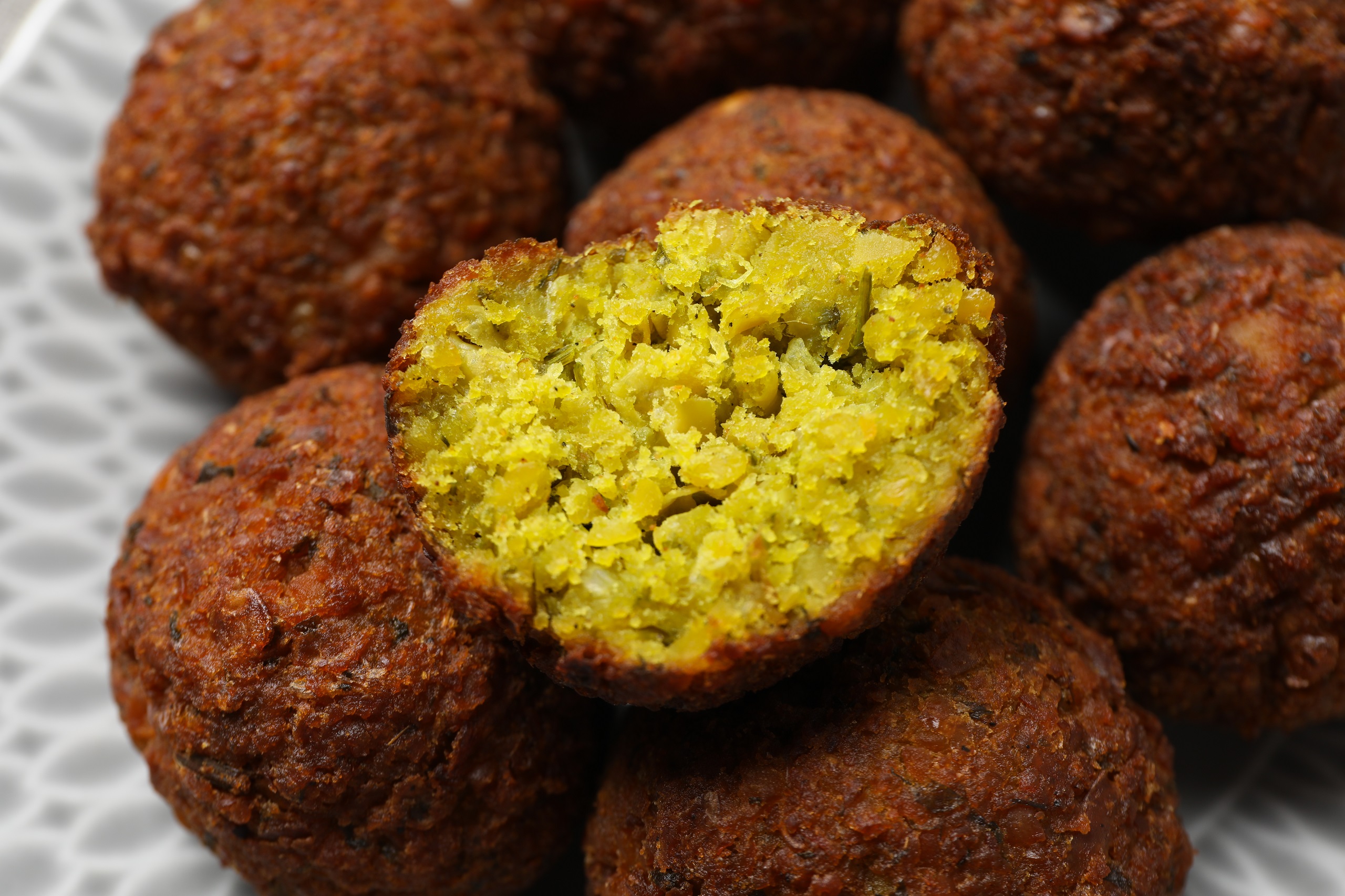 Crunchy falafel balls piled up on a fancy plate with half a falafel ball on the top depicting the soft chickpea filling inside.