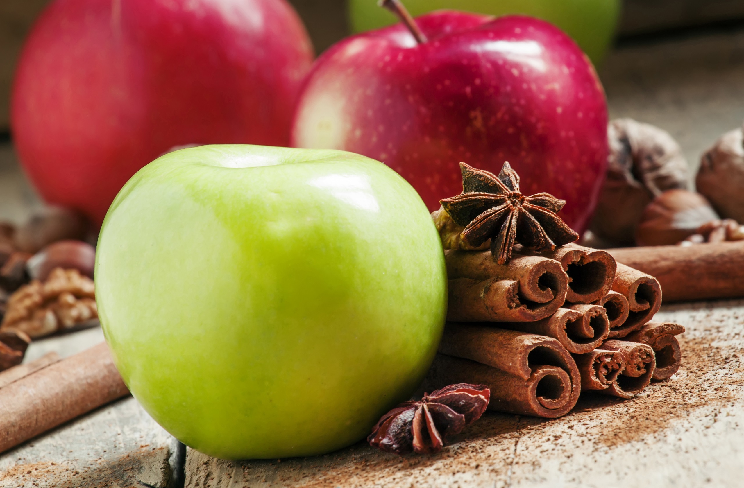 Juicy red and green apples with cinnamon sticks, grounded cinnamon, anise stars, walnuts and hazelunts, on a rustic wooden background.
