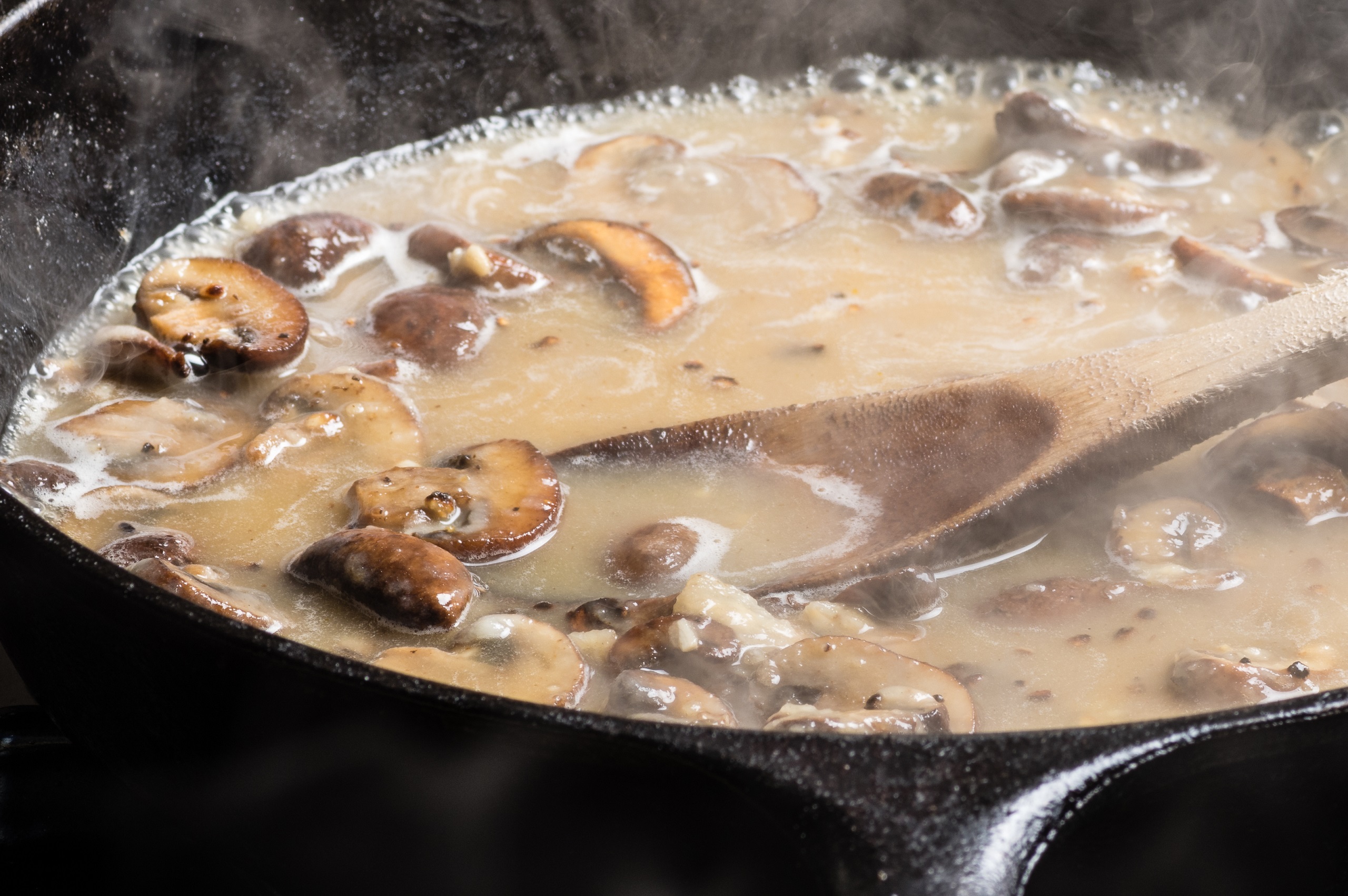 Hot simmering mushroom gravy or rue still in the iron skillet with a big wooden spoon as if to pour the sauce.