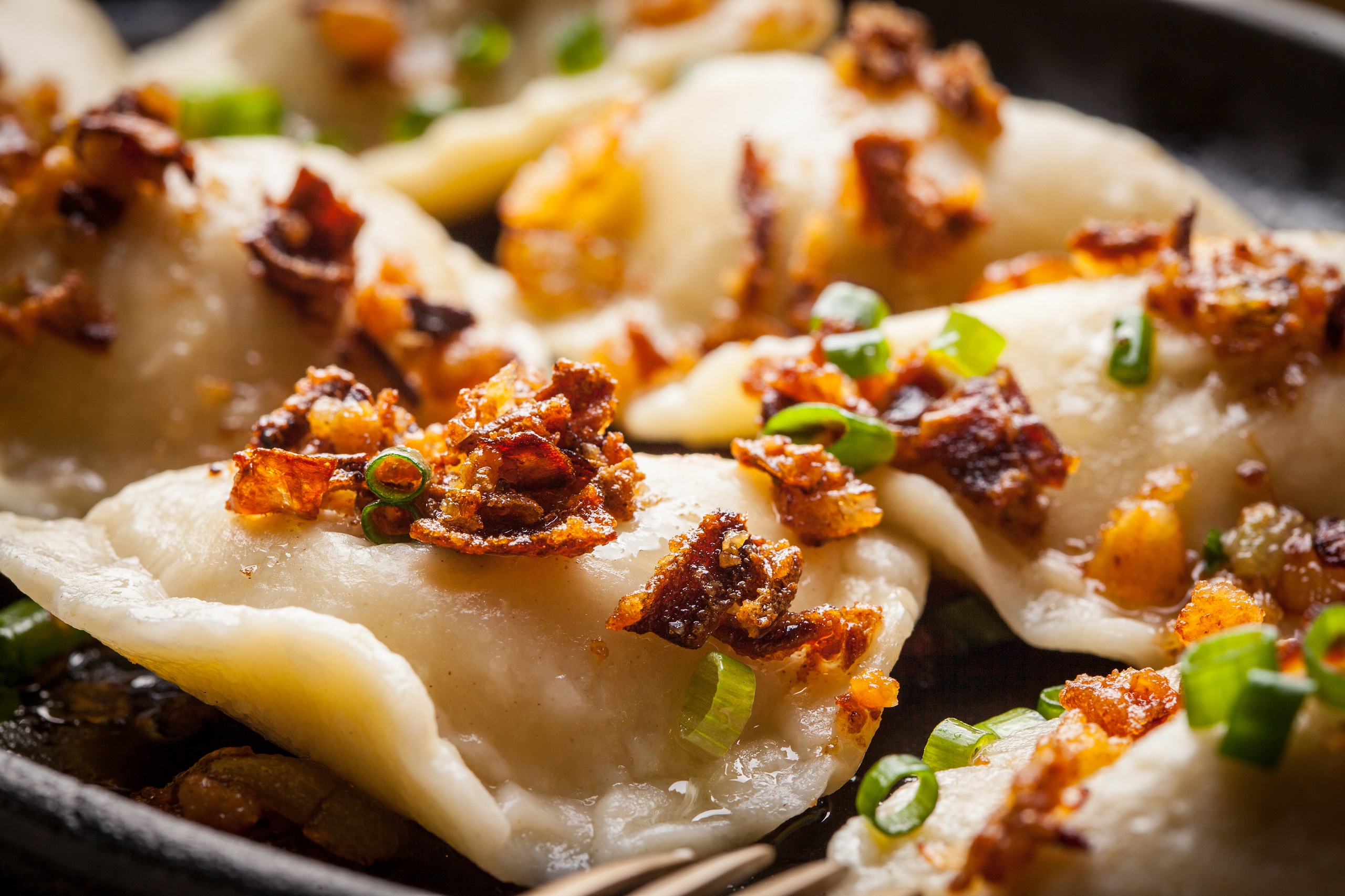 A close up of Polish pierogies garnished with bacon and onions in a cast iron skillet.