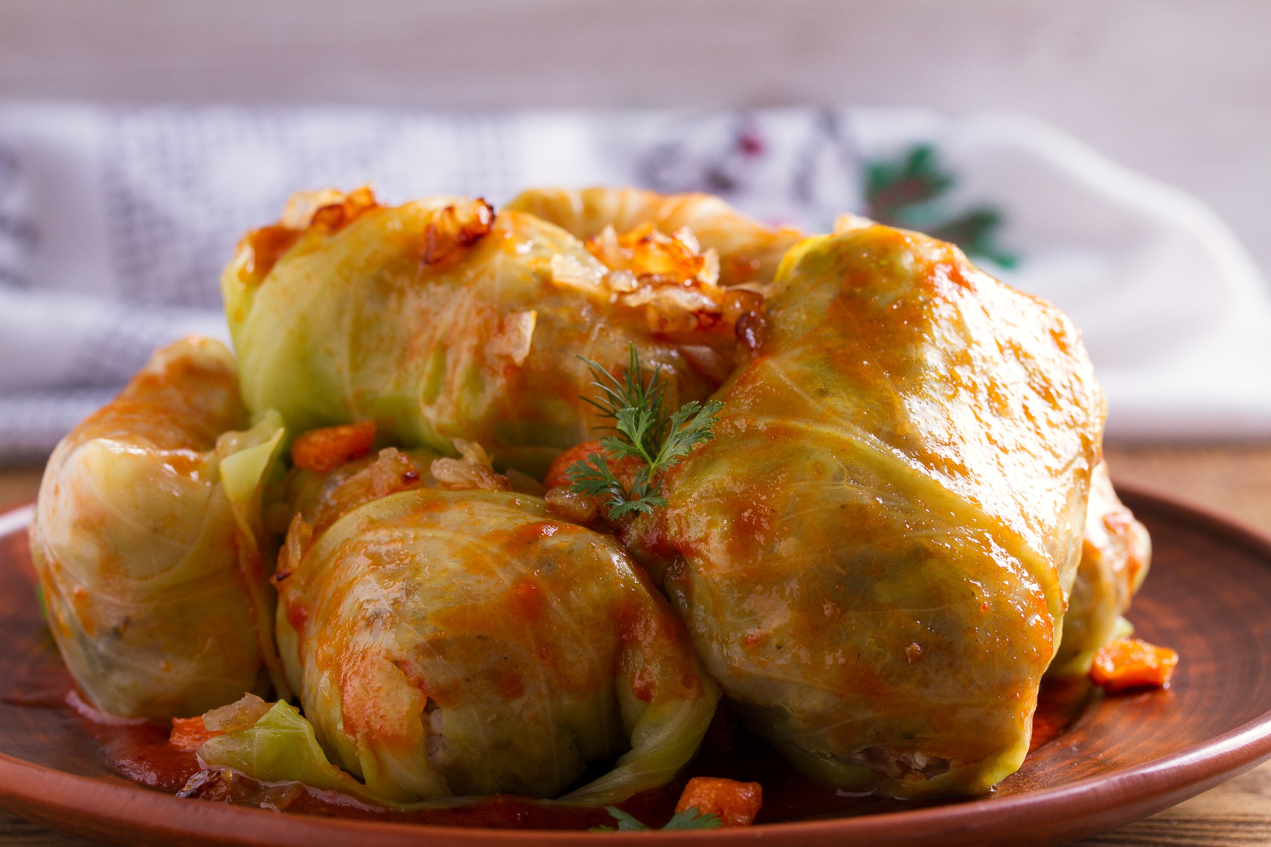 Stuffed cabbage rolls filled with sautéed ground meats, cooked rice, and roasted vegetables, stacked on a brown plate and garnished with parsley.