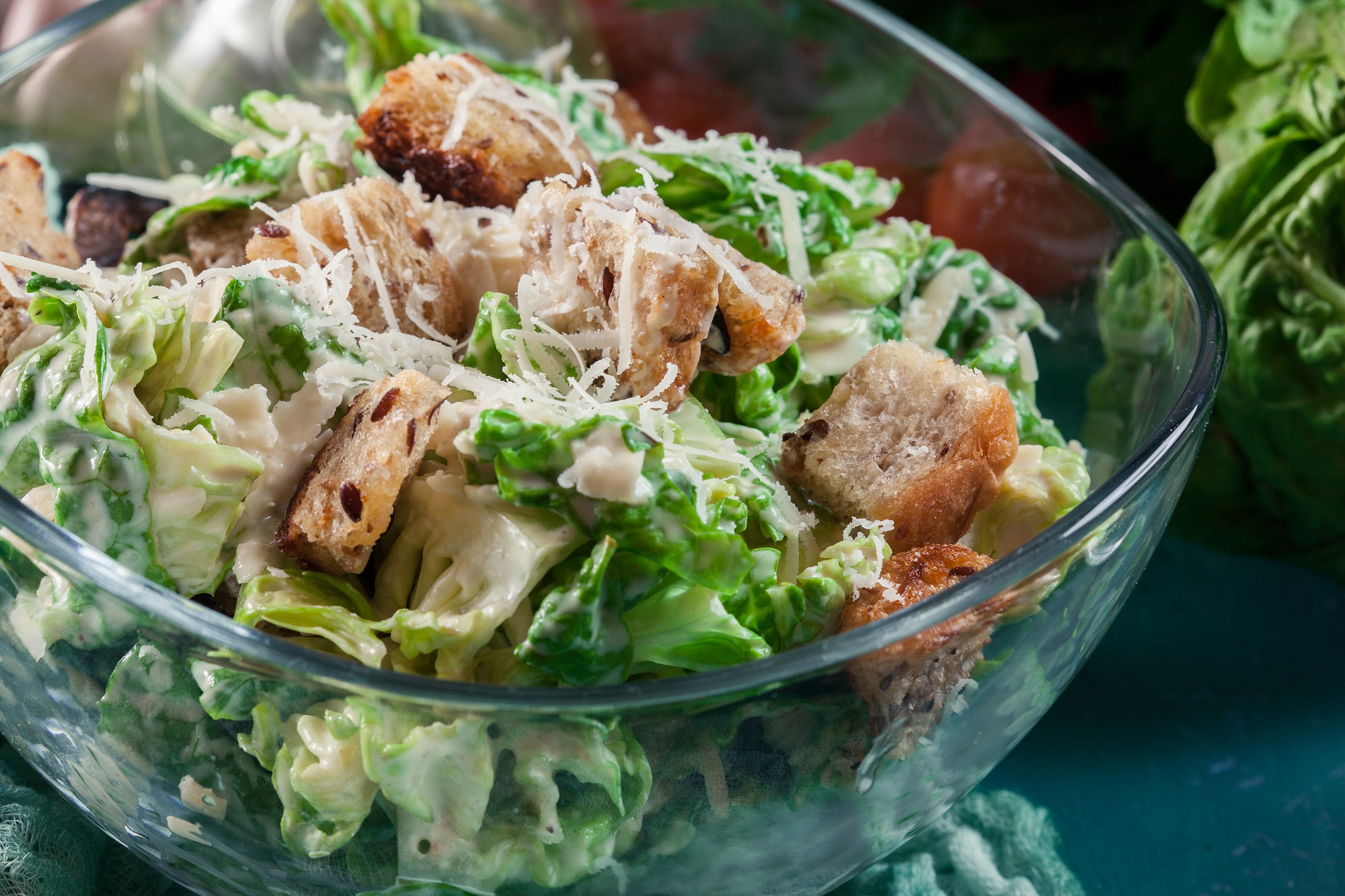 Caesar salad with parmesan cheese shavings and crunchy croutons with homemade caesar dressing in a clear salad bowl.