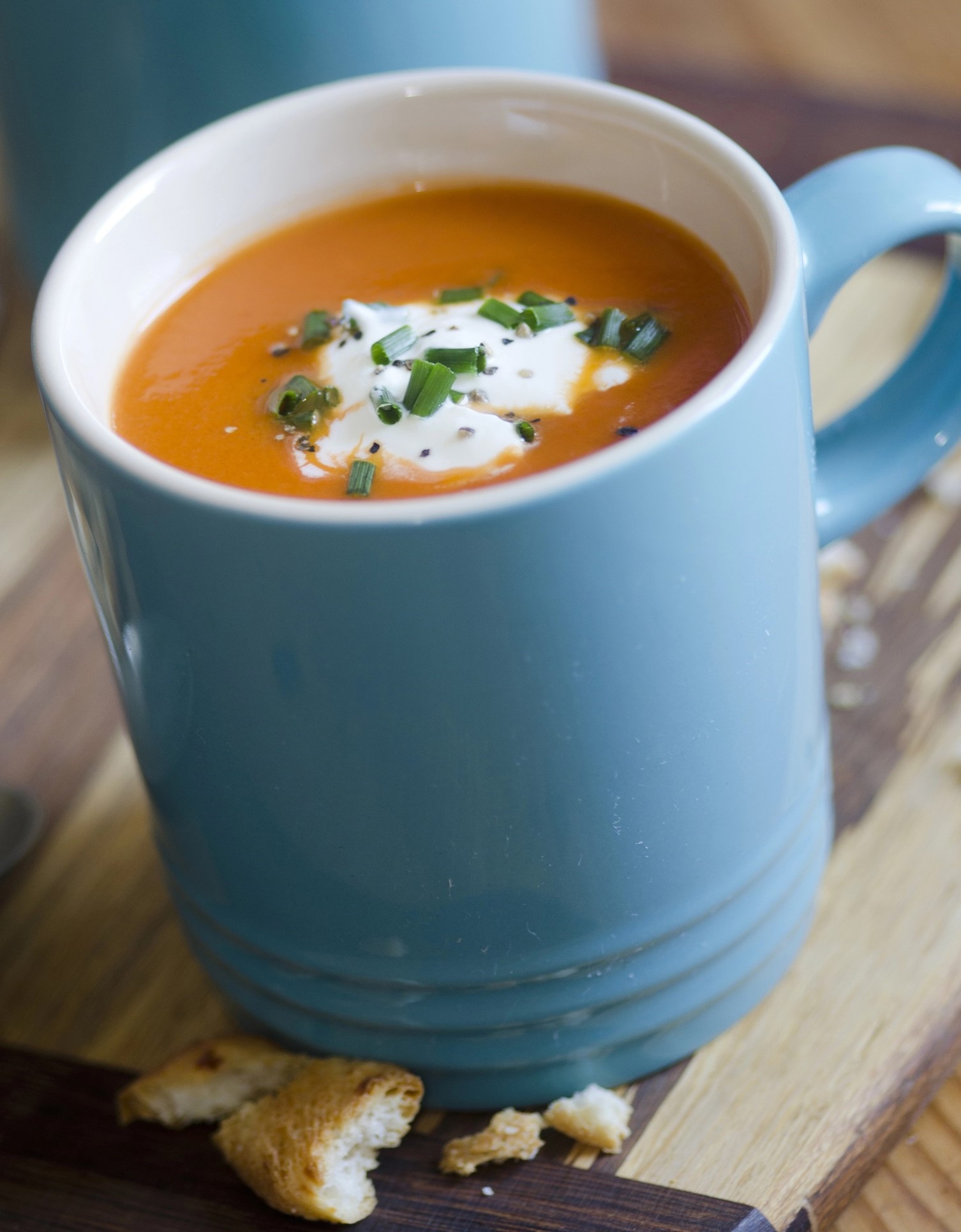 Creamy Tomato Soup in blue mugs with handle on a wood board.