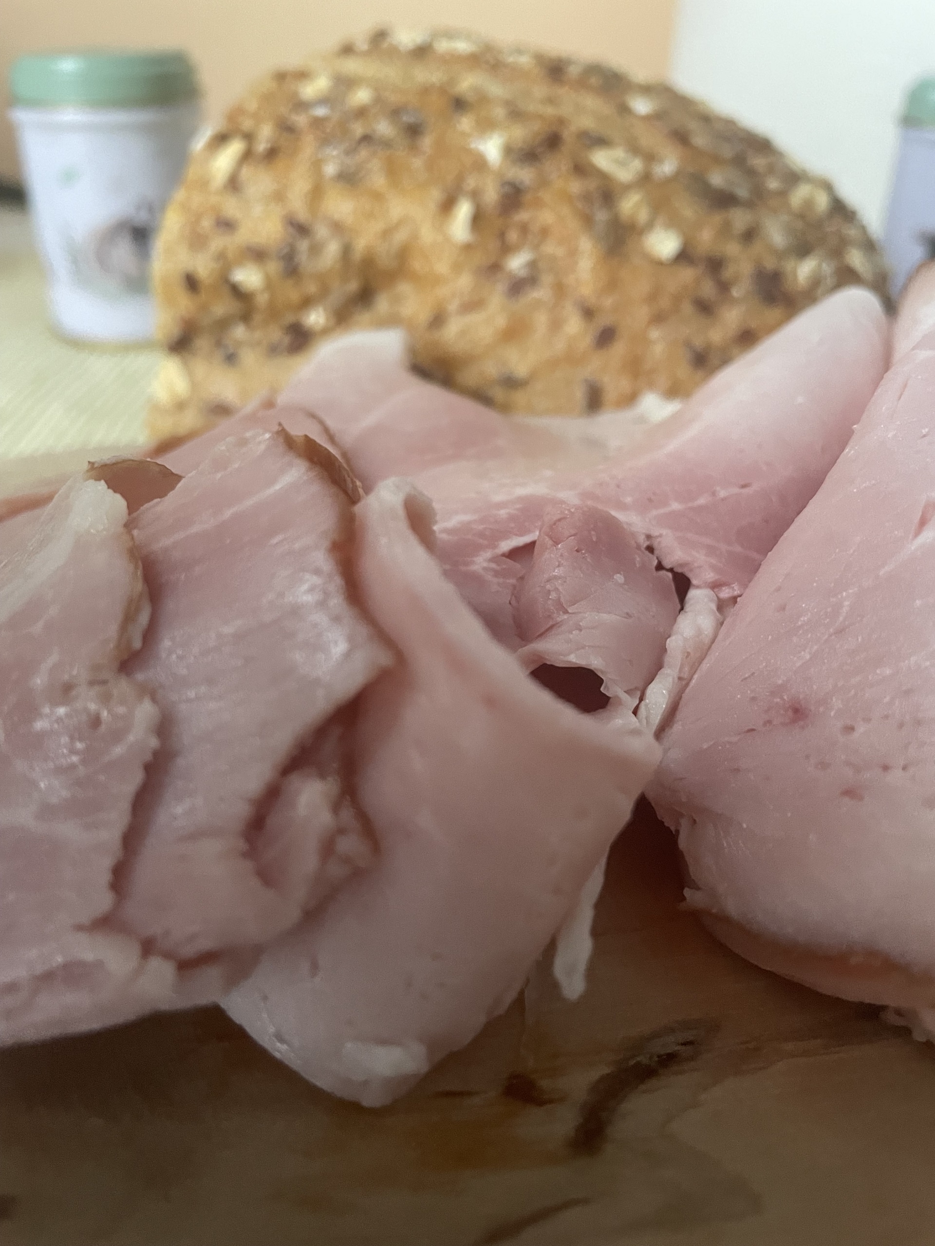 Slices of Polish ham right off the bone with a multigrain loaf of bread in the background, closeup.