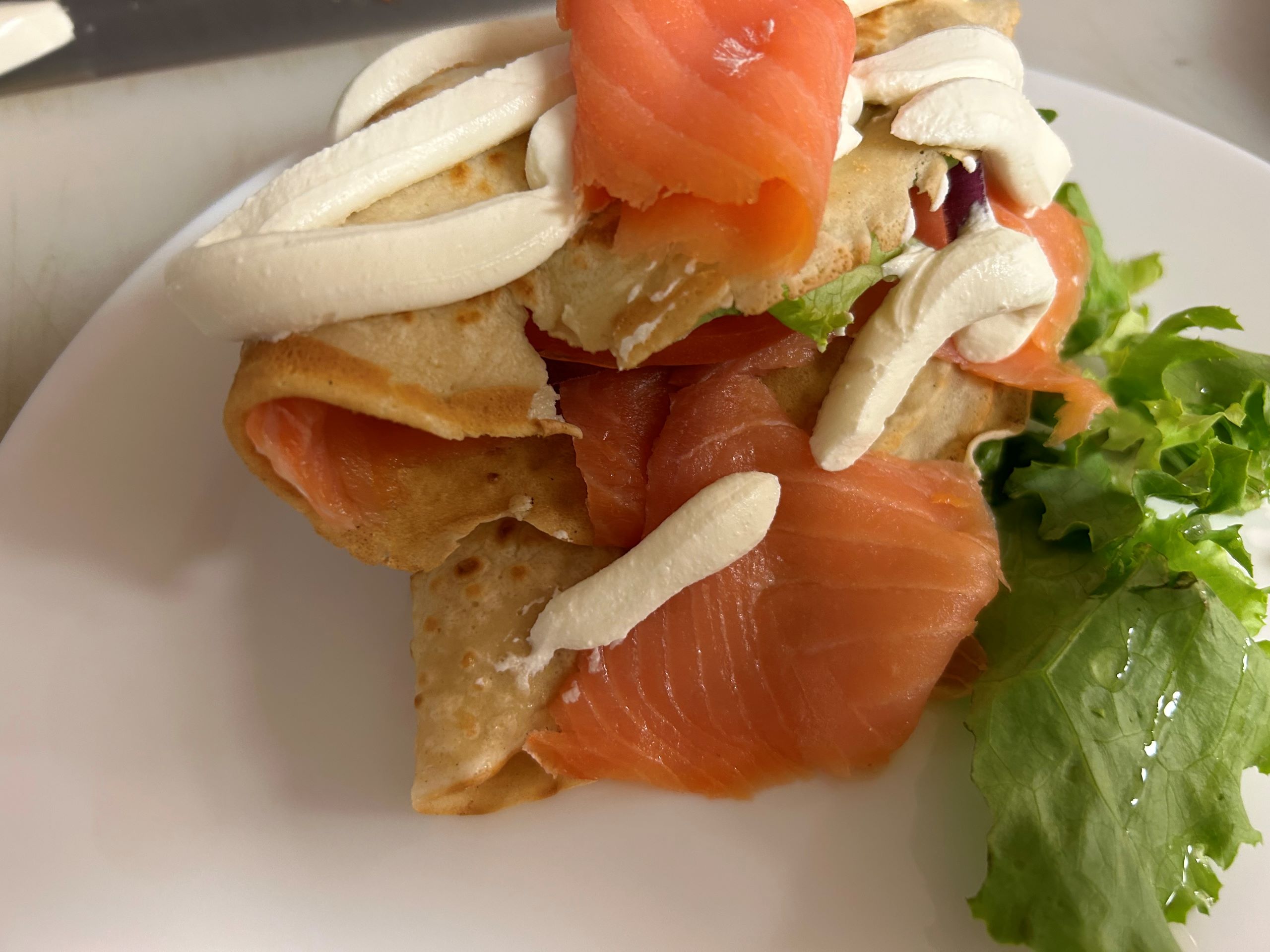 Slices of Smoked Salmon and Cream Cheese Spread artfully wrapped in a blintz pancake with crispy lettuce and slices of tomatoes, red onions, on a white plate, close up.