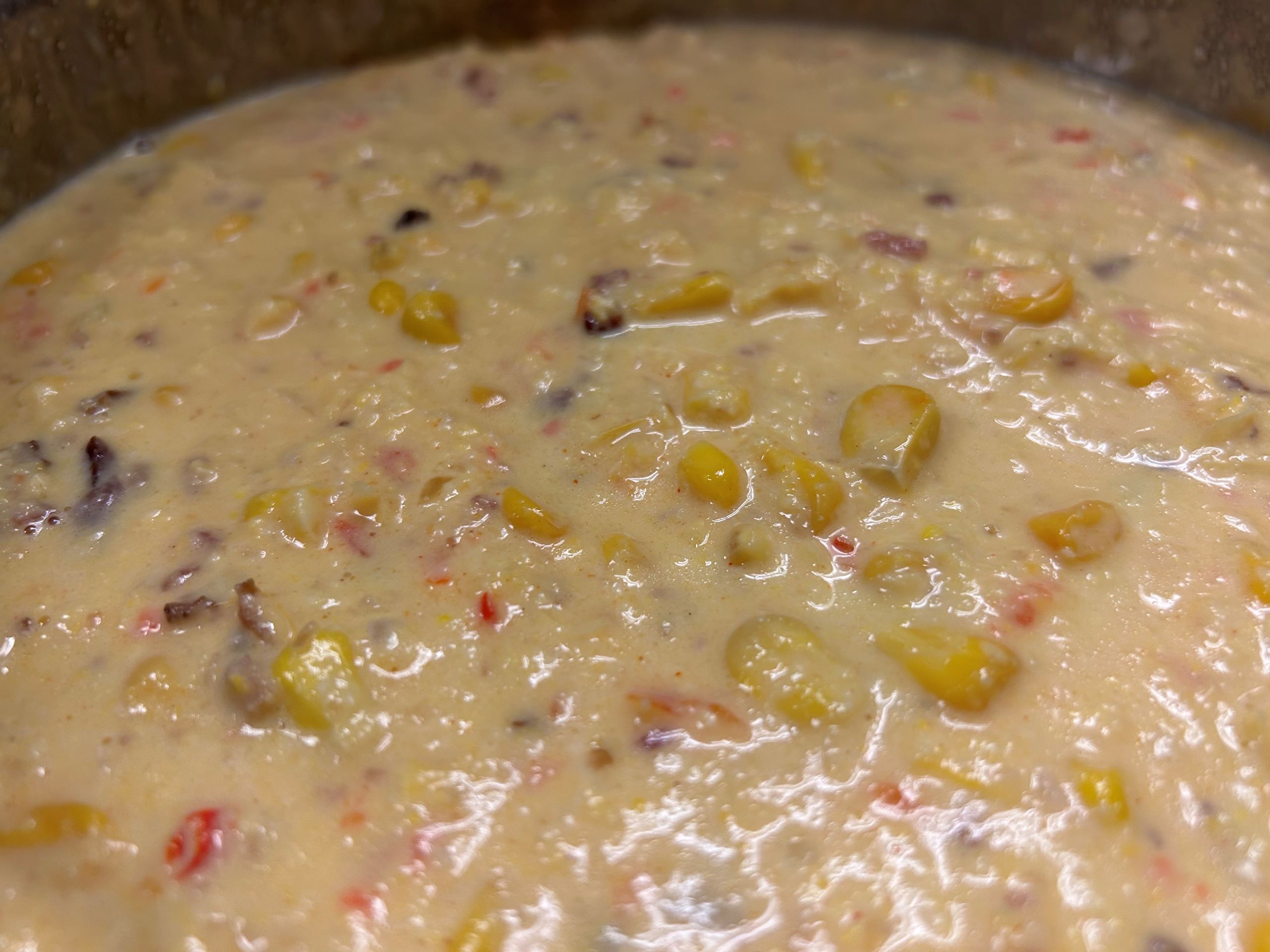Kat's Creamy Bacon Corn Chowder Soup still in the pot with visible sweet corn pieces, thin sliced vegetables, in a steel pot, close up.