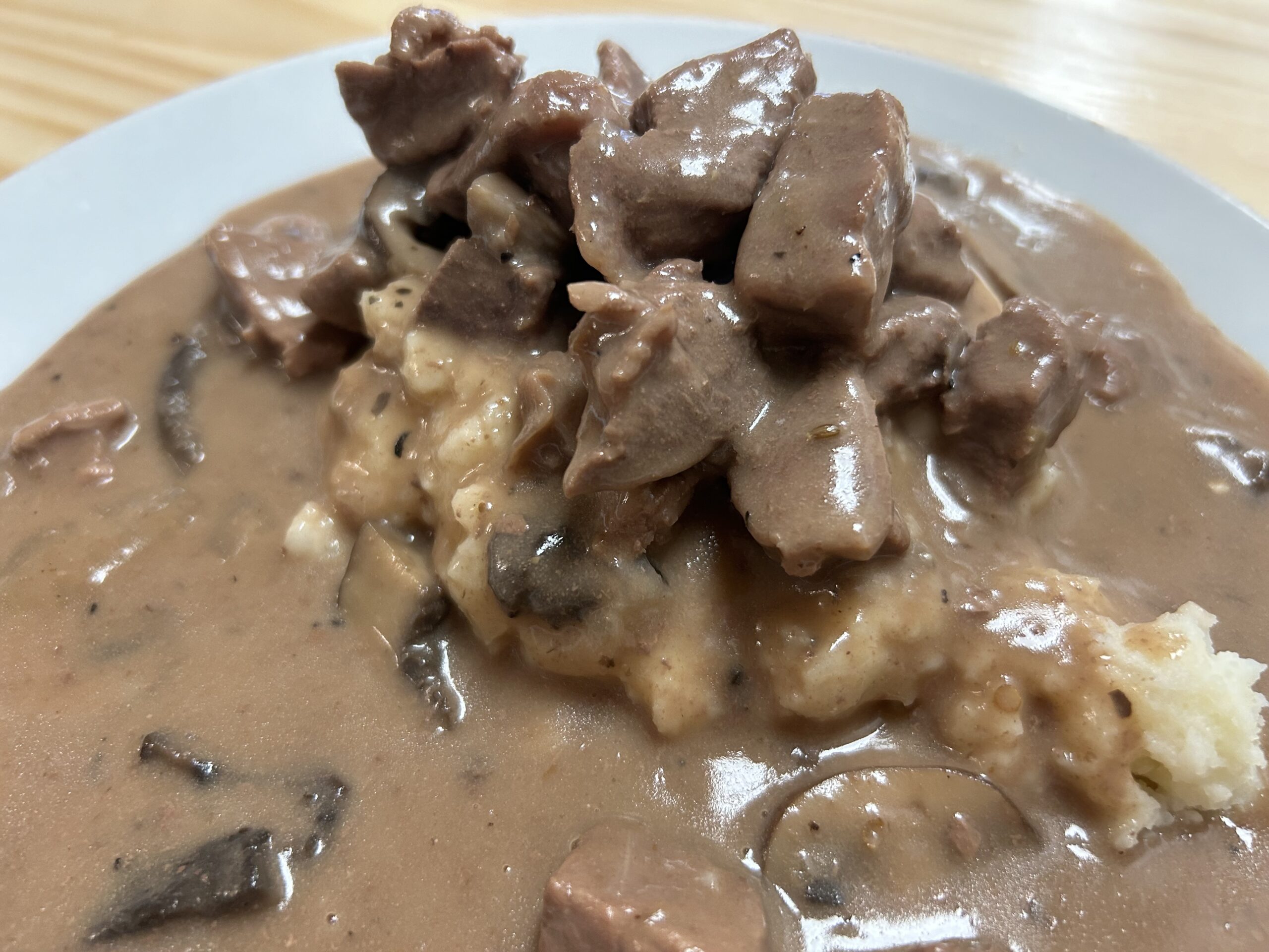 Kat's Beef Stroganoff made in Red Wine on a white plate in its creamy mushroom sauce and a serving of mashed potatoes on a wood ash table.