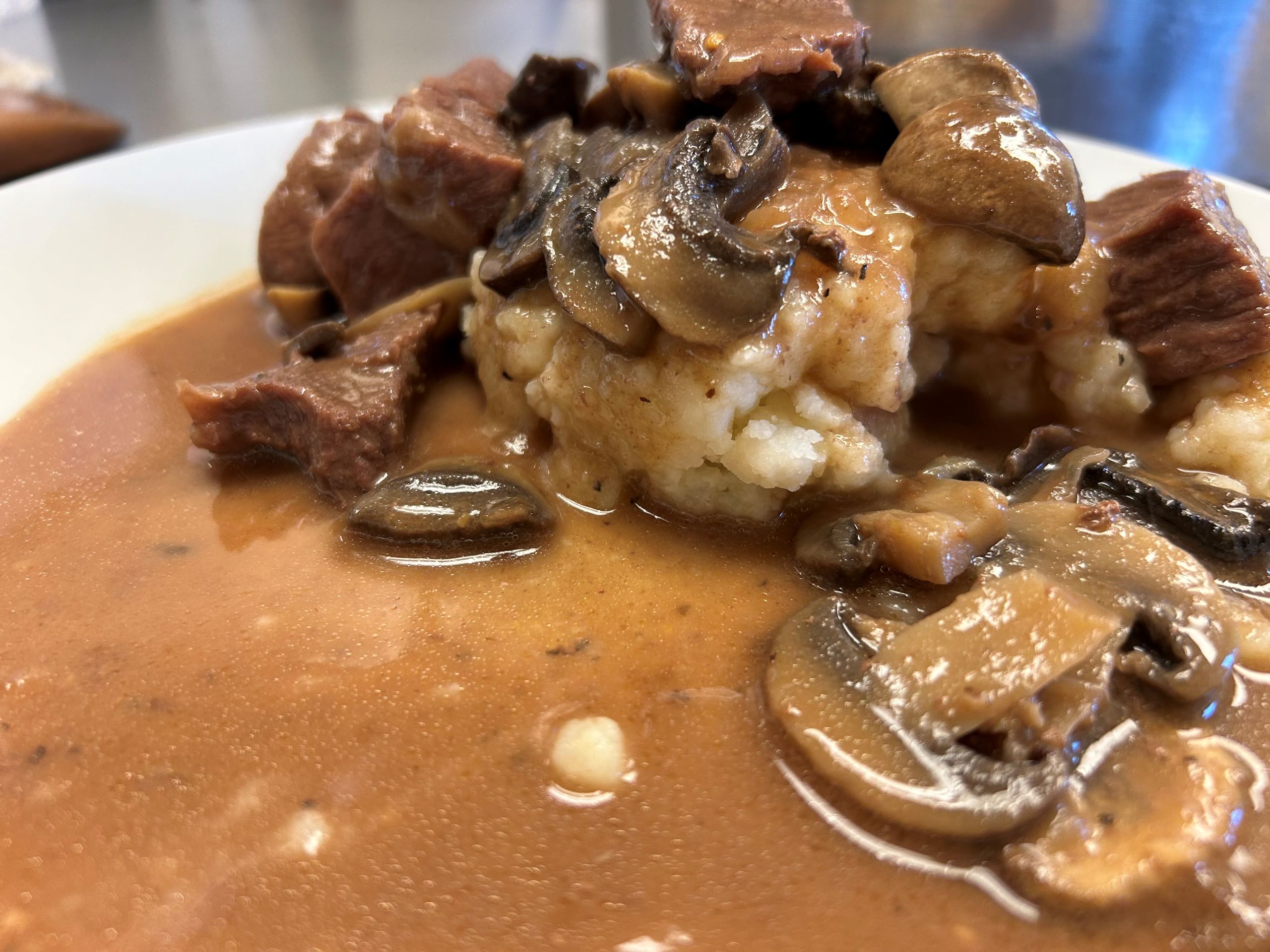 Kat's Coffee Infused Pork slow cooked in chardonnay and mushroom flavored served with sliced and whole mushrooms on mashed potatoes on a white plate.