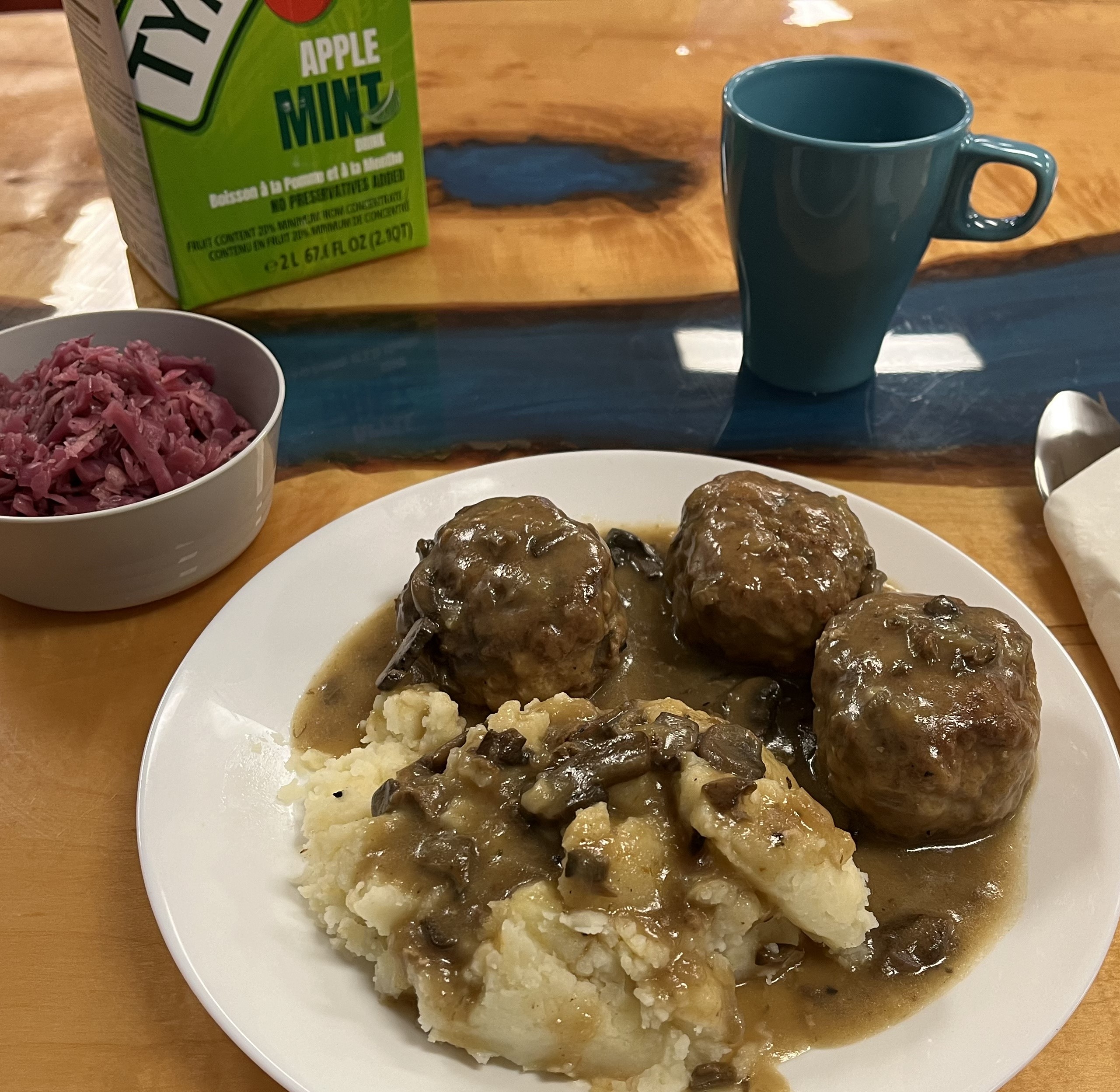 Kat's homemade meatballs with mashed potatoes and mushroom gravy sauce served on a white plate with a side bowl of Slavic house vegetable salad.