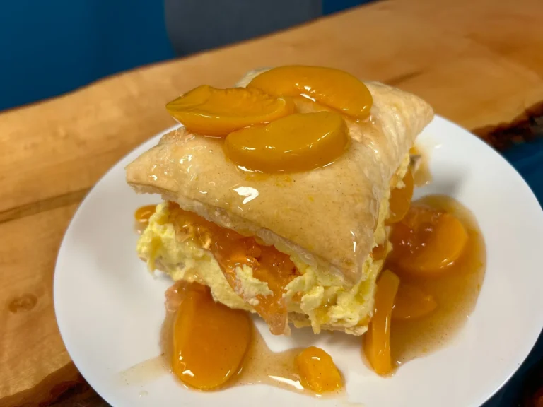 Slavic Napoleon dessert at Kat’s Café & Restaurant layered with homemade cream and peaches, topped with natural peach sauce and cinnamon on a white plate.