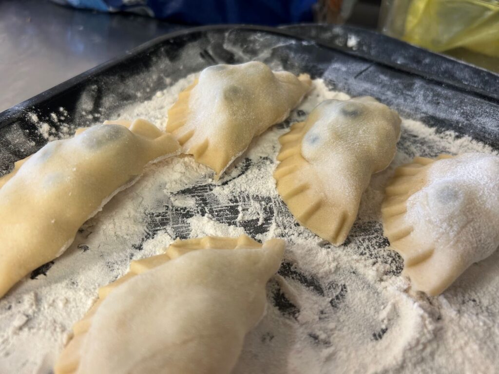 Kat's Fresh Blueberry Pierogies on a Black Tray with Flour on a Stainless Steel Surface.