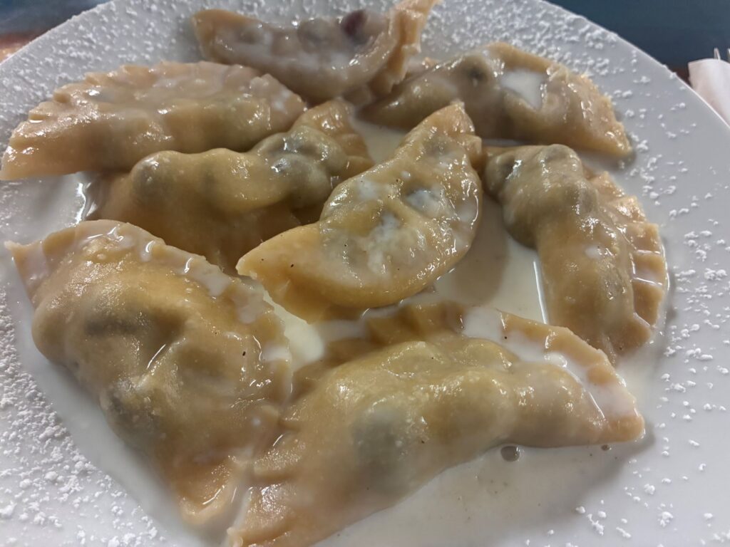 Kat's Seasonal Blueberry Pierogies Served on a White Plate with Homemade Cream and a Sprinkle of Sugar.