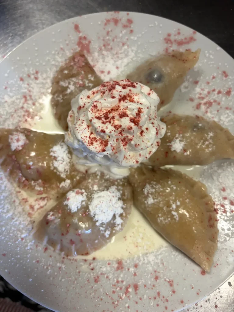 Overhead view of handmade blueberry pierogies served with whipped cream, powdered sugar, and berry-colored decorative sugar at Kat’s Café