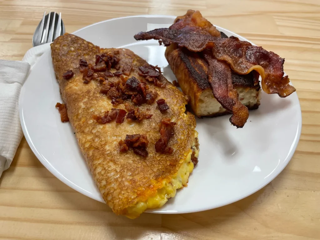 Bacon, egg, and cheese blintz served on a breakfast plate with bacon and a savory potato babka side at Kat’s Café & Restaurant.
