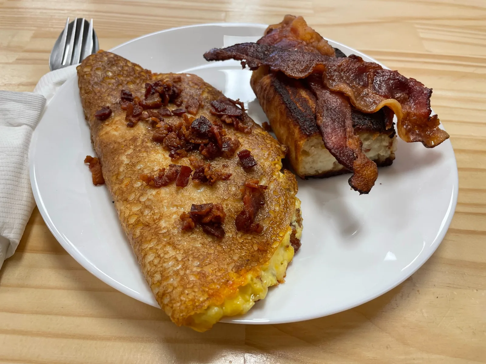 Bacon, egg, and cheese blintz served on a breakfast plate with bacon and a savory potato babka side at Kat’s Café & Restaurant.