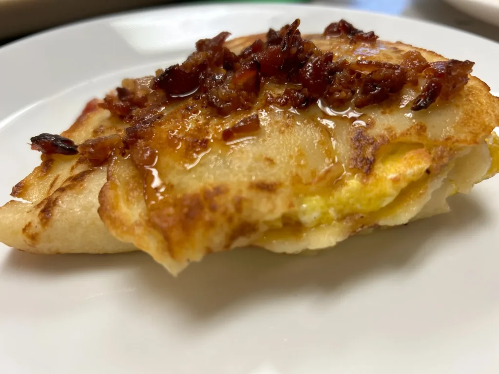 Close-up of a bacon, egg, and cheese crepe topped with crisp bacon at Kat’s Café & Restaurant.