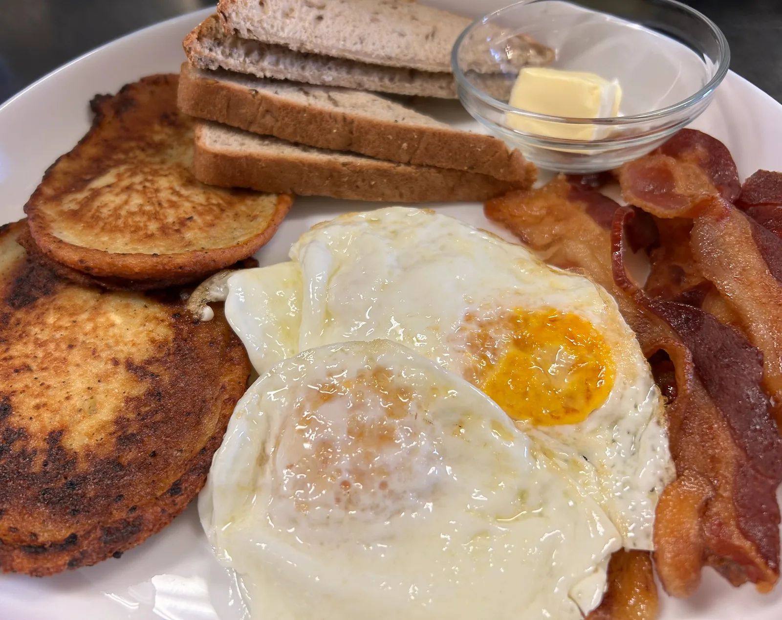 Close view of browned potato bleenies beside fried eggs and bacon, with toast and butter at the back of the breakfast plate at Kat’s Café & Restaurant.