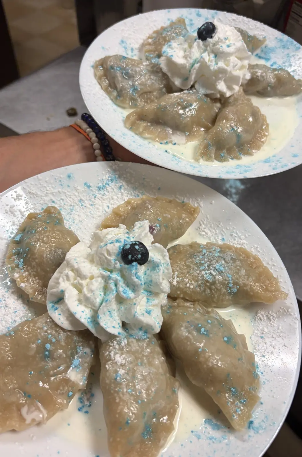 Two plates of handmade seasonal blueberry pierogies served with cream, whipped cream, powdered sugar, blue decorative sugar, and fresh blueberries at Kat’s Café & Restaurant.