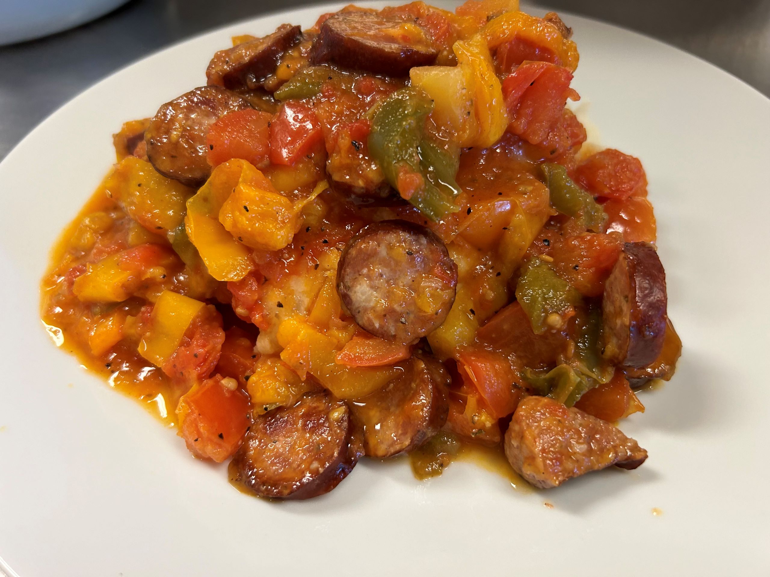 Kat's Letcho Kielbasa Meal having pan-fried kielbasa pieces, sauteed onions and fresh peppers all together on mashed potatoes served on a white plate.