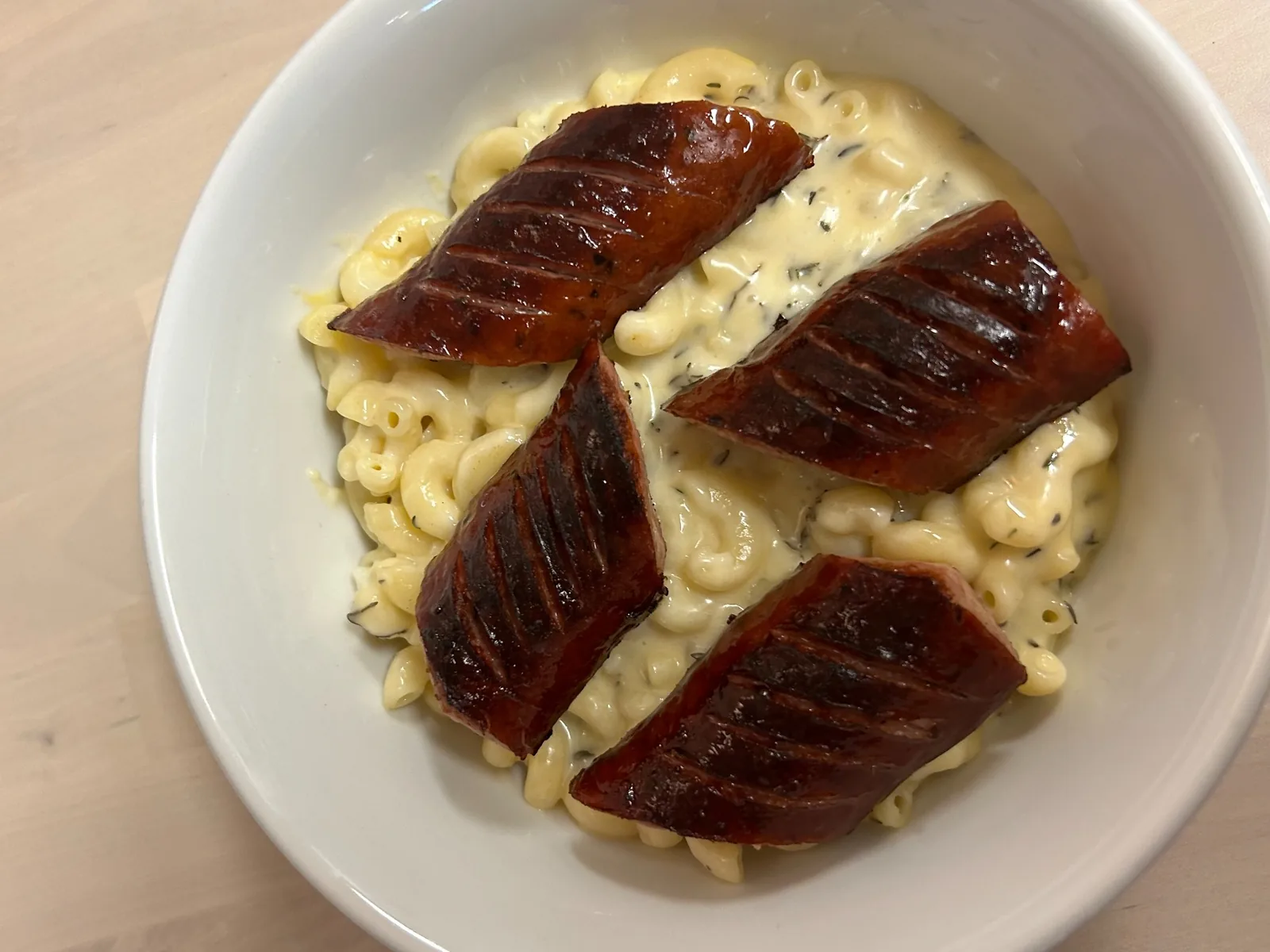 Four thick pieces of browned, pan-fried kielbasa over creamy homemade macaroni and cheese at Kat’s Café & Restaurant, viewed from above in a white bowl on a wooden table.