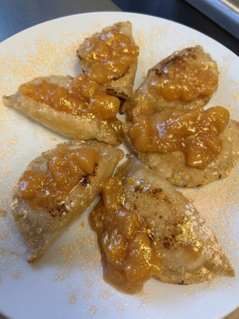Peach Pierogies topped with homemade chunky peach syrup served on a white plate sprinkled with pink sugar glaze.
