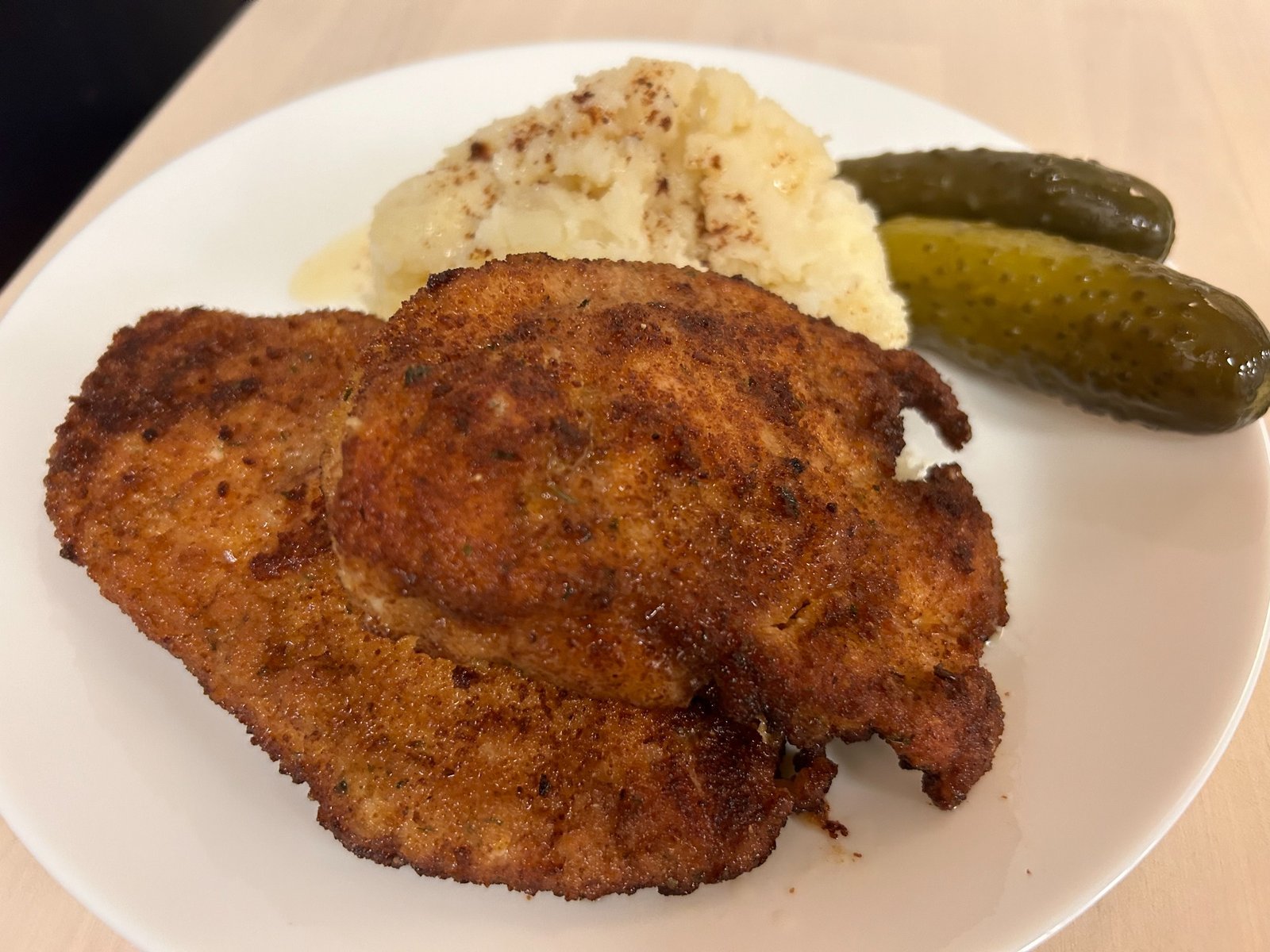 Two overlapping golden breaded chicken cutlets with mashed potatoes and pickles behind them, served on a white plate for lunch or dinner at Kat’s Café & Restaurant.