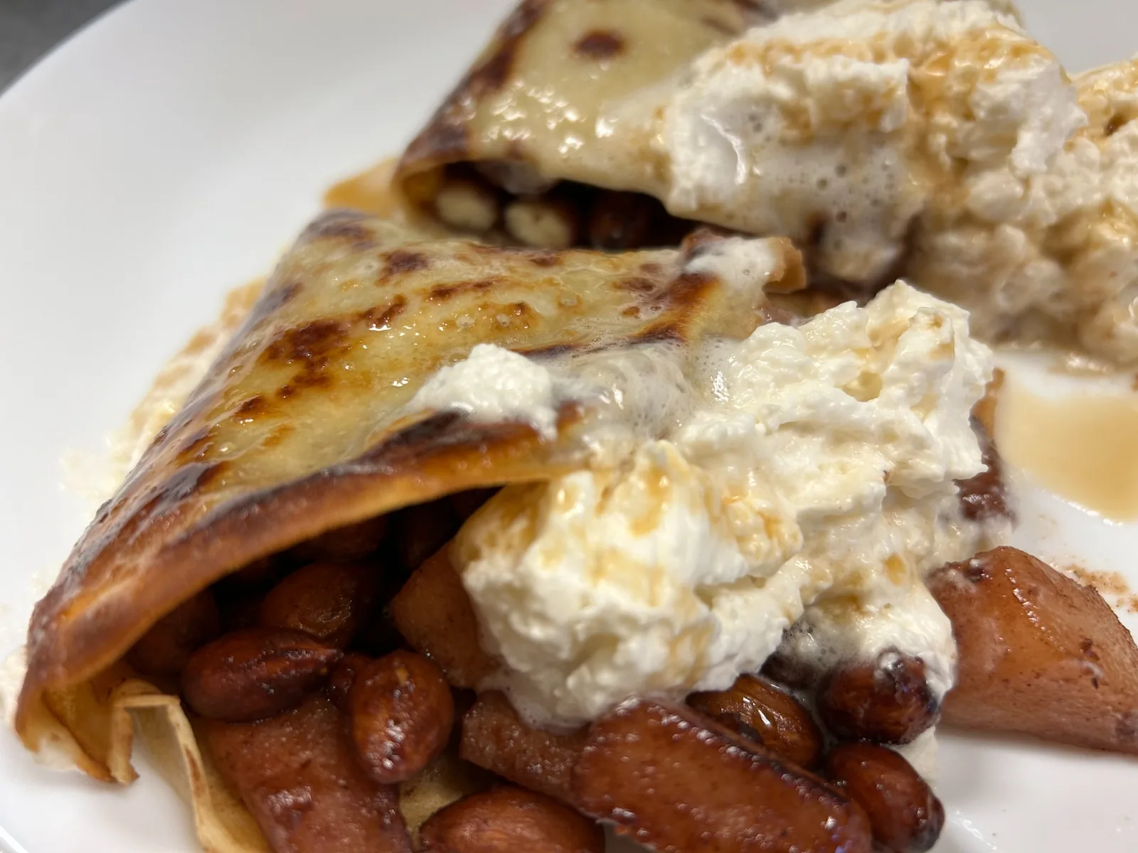 Close-up of a browned crepe dessert with a caramelized pear-almond filling, topped with whipped cream and a light sweet maple glaze at Kat’s Café & Restaurant.