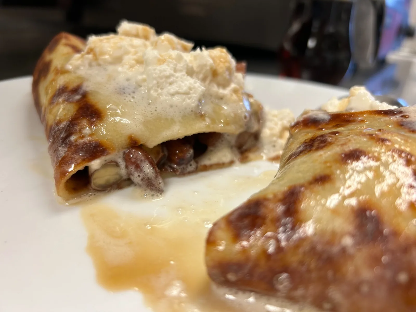 Close-up of two halves of a warm crepe filled with a sweet, caramelized orchard pear filling and almonds, topped with whipped cream and a maple glaze on a white plate at Kat’s Café & Resaurant.