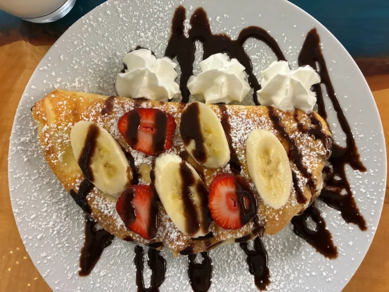 Dessert crepe filled with vanilla sweet cheese and topped with strawberries, bananas, whipped cream, powdered sugar, and chocolate sauce at Kat’s Café & Restaurant.
