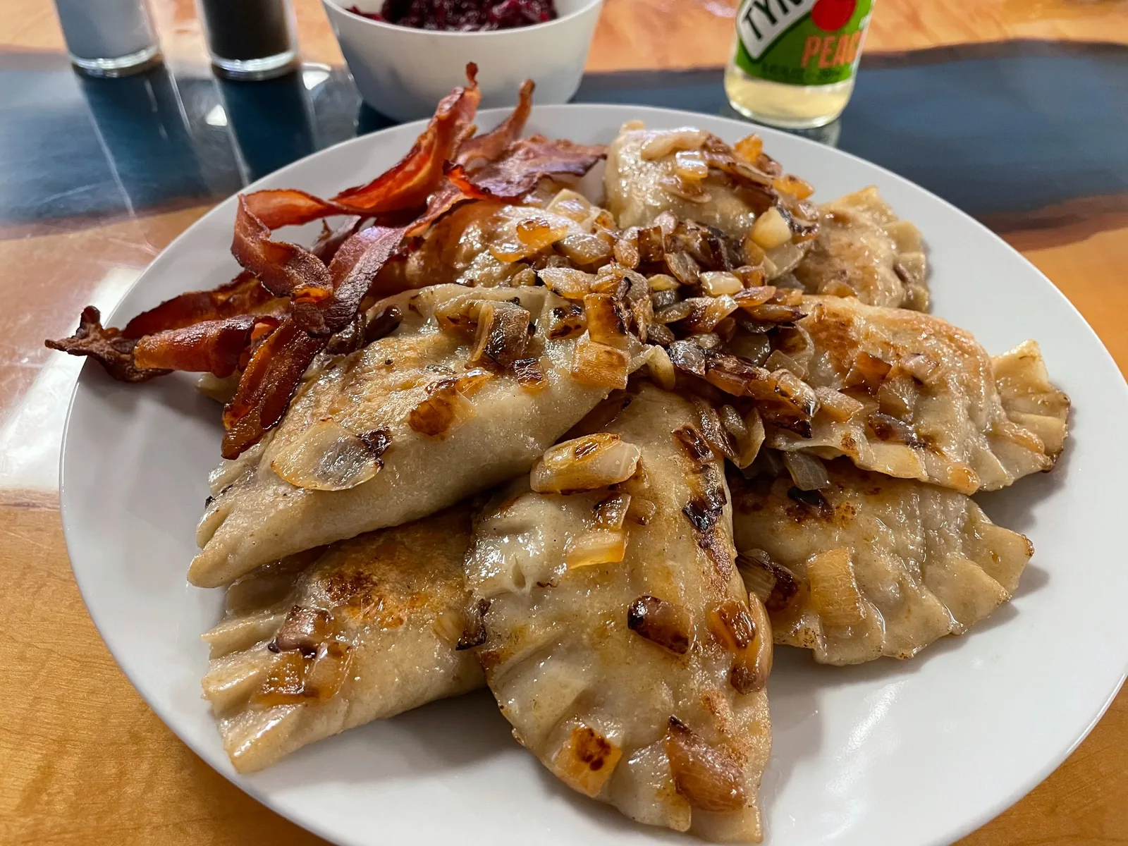 Pan-fried homemade meat pierogies at Kat’s Café & Restaurant, topped with caramelized onions and served with crisp bacon strips on a white plate.