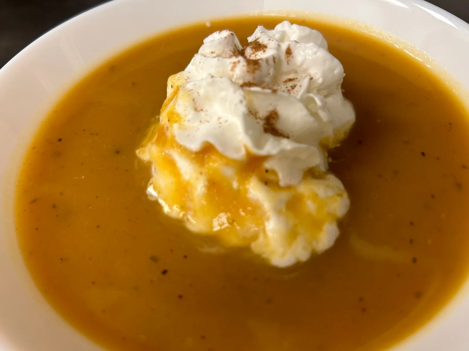 Close-up of creamy pumpkin soup topped with maple-infused whipped cream and cinnamon at Kat’s Café & Restaurant.
