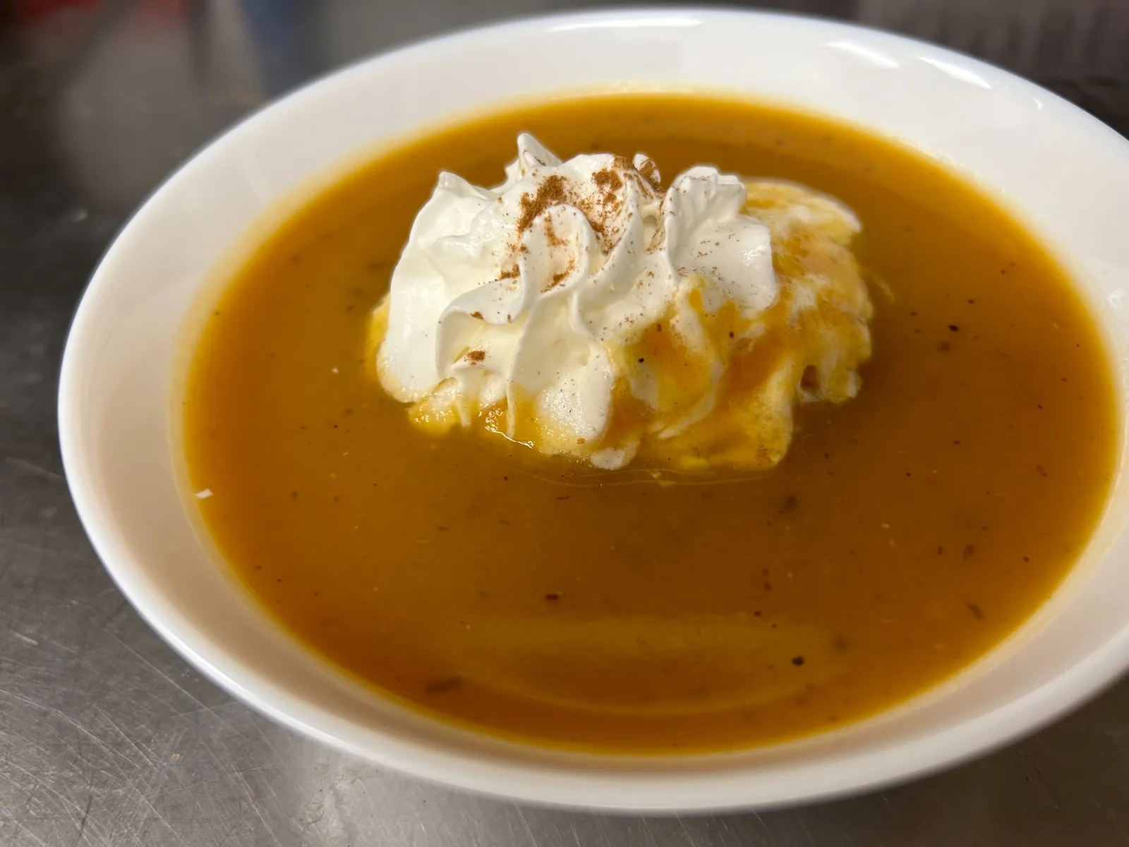 Creamy pumpkin soup topped with maple-infused whipped cream and a dusting of cinnamon in a white bowl at Kat’s Café & Restaurant.