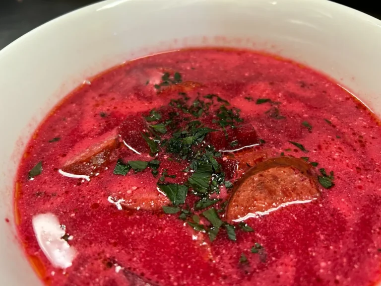 Red beet borscht with smoked kielbasa and chopped herbs in a white bowl at Kat’s Café & Restaurant.