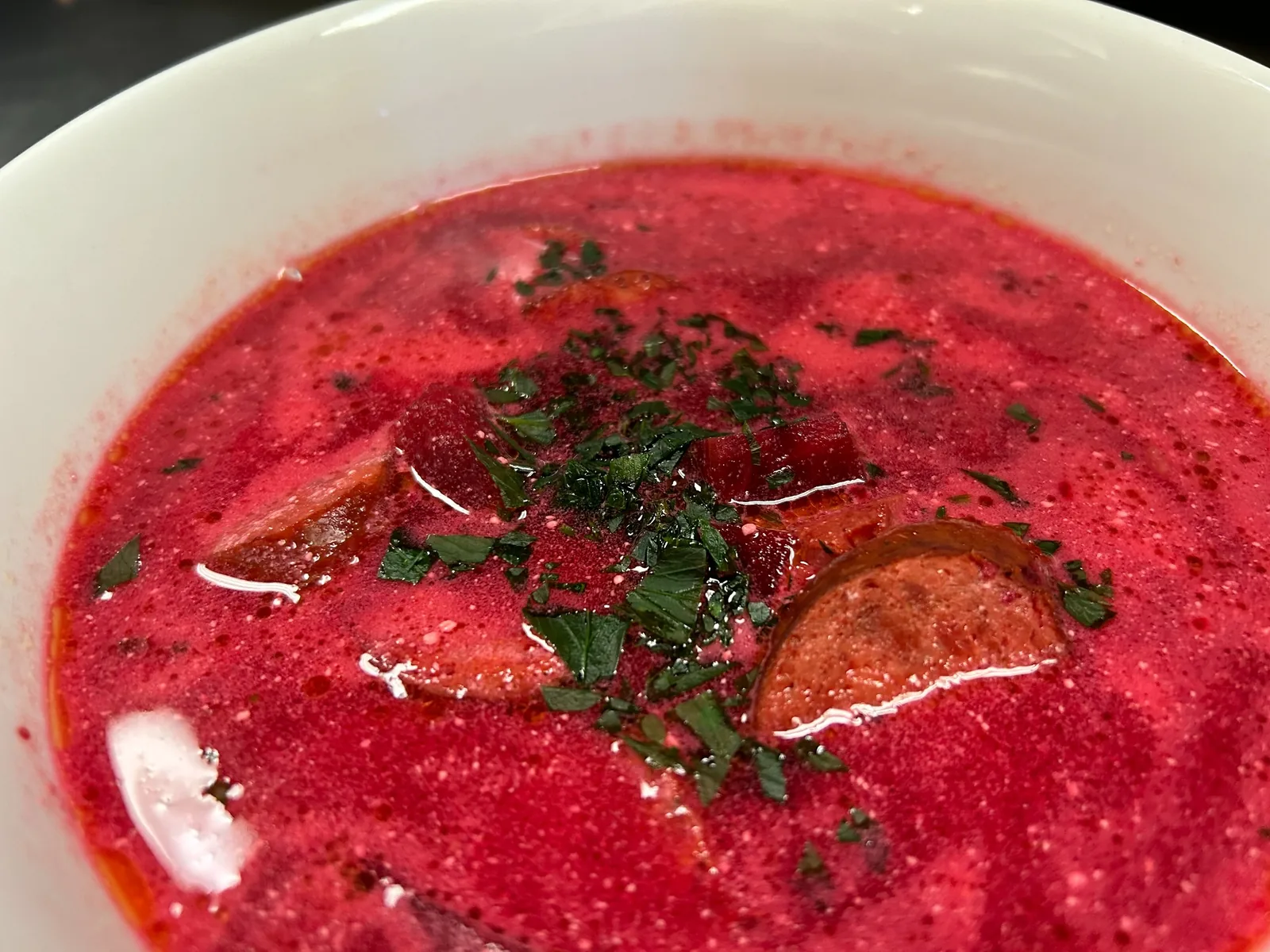 Red beet borscht with smoked kielbasa and chopped herbs in a white bowl at Kat’s Café & Restaurant.