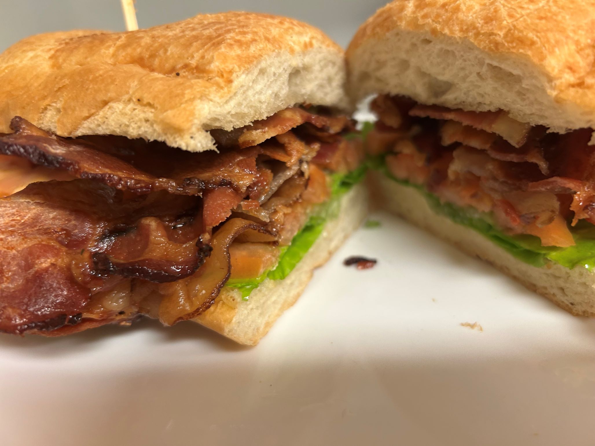 Kat's BLT Sub cut in half showing a generous layer of bacon, lettuce, and tomato with a tooth pick in each half holding the sandwich together, served on a white plate.