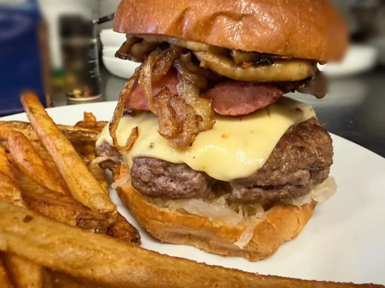 Close-up of Kat’s Kielbasa Burger with a beef smash patty, grilled kielbasa, melted cheese, caramelized onions, and homemade sauerkraut on a toasted bun, served with fries at Kat’s Café & Restaurant.