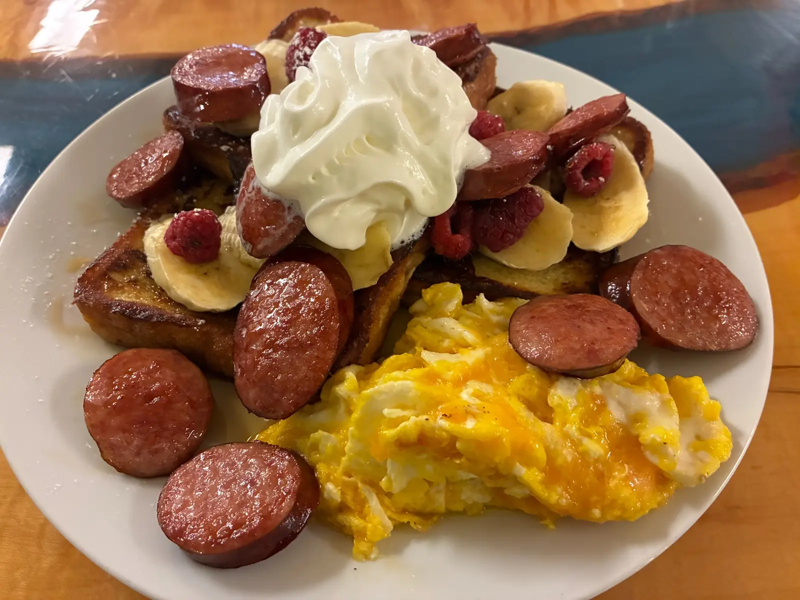 French toast topped with bananas, raspberries, bacon, and whipped cream, served with scrambled eggs and sliced kielbasa at Kat’s Café & Restaurant.