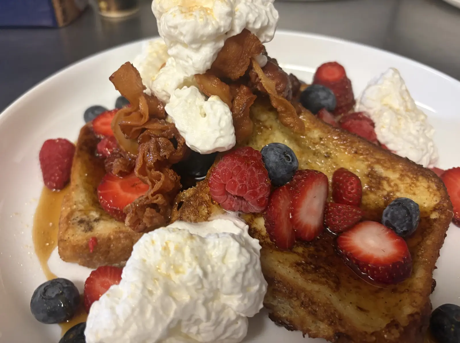 French toast topped with strawberries, blueberries, raspberries, bacon, and whipped cream on a white plate at Kat’s Café & Restaurant.