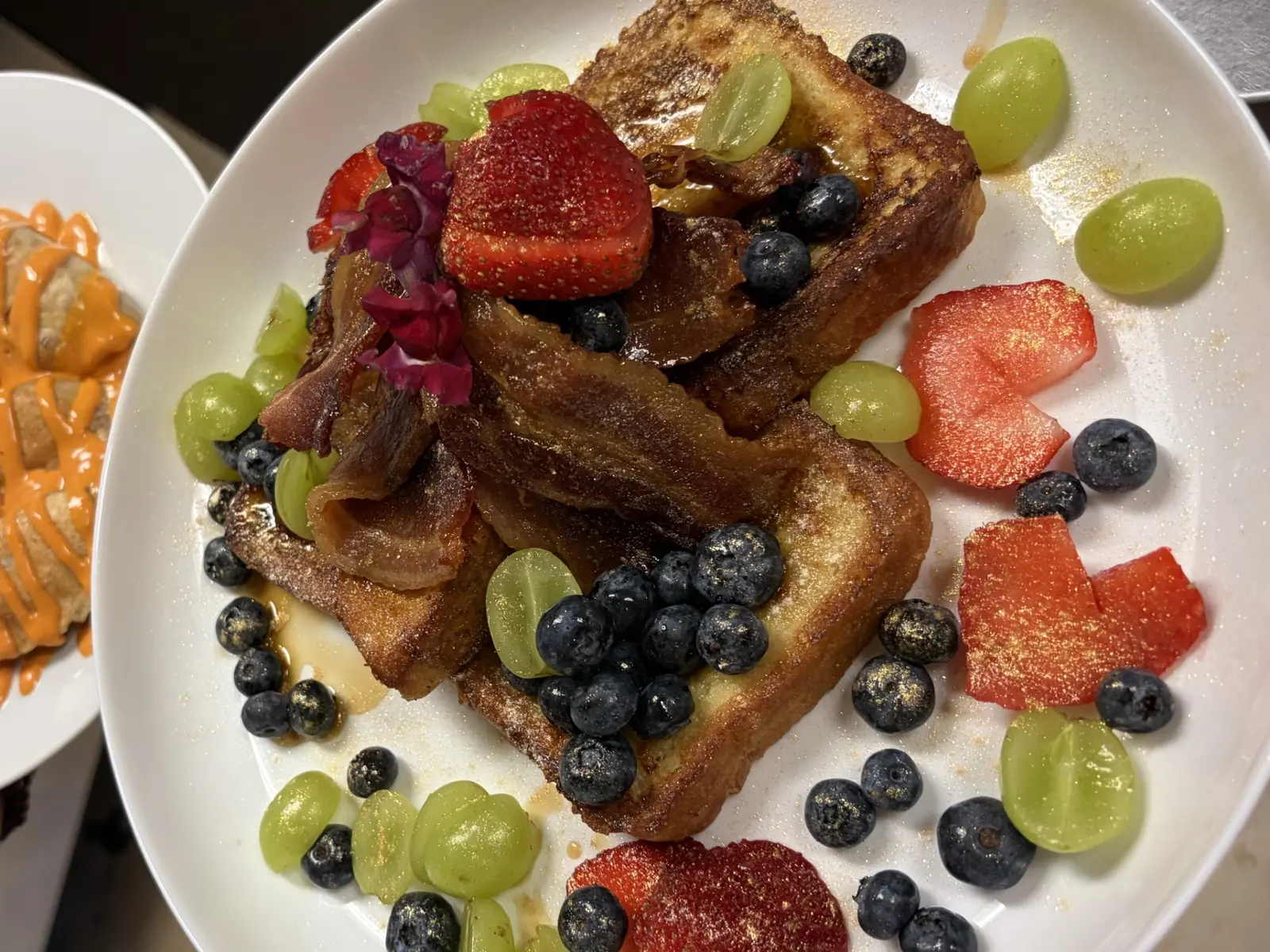 Overhead view of French toast topped and surrounded by strawberries, blueberries, grapes, bacon, and powdered sugar at Kat’s Café & Restaurant.