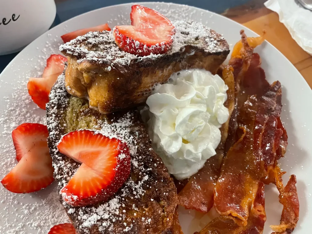 Kat’s Café & Restaurant French toast dusted with powdered sugar and served with sliced strawberries, whipped cream, and maple-glazed bacon.