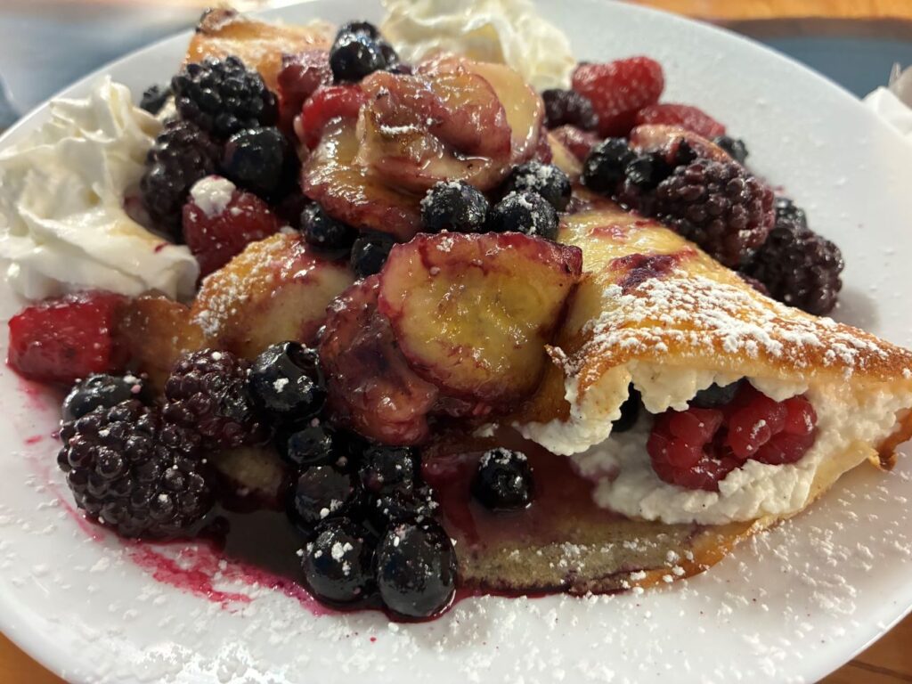 Vanilla Sweet Cheese Fruit Crepe Wonders having caramelized fruit topping over an ultra-light folded crepe with vanilla sweet cheese filling and fruits, served on a white plate with homemade whipped cream and sprinkled with powdered sugar.