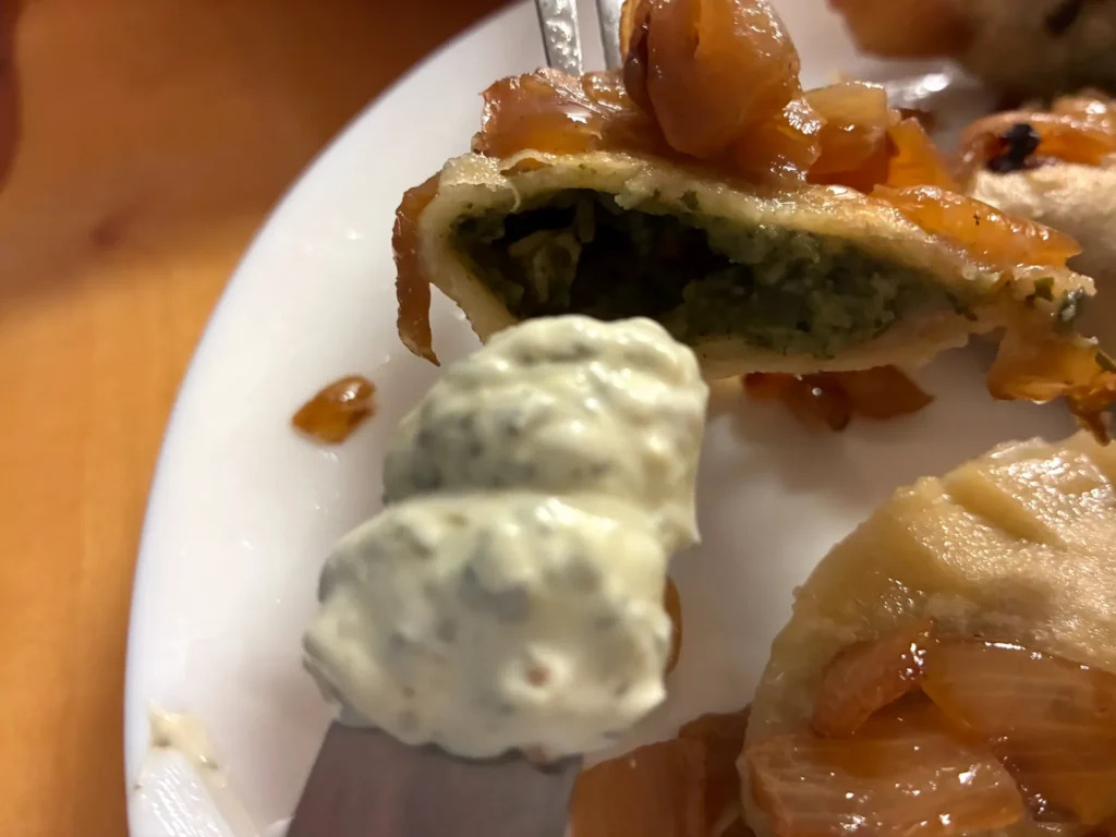 Tight close-up of a spinach and feta cheese pierogi cut open to show the filling, with caramelized onions and creamy artichoke dip at Kat’s Café & Restaurant.