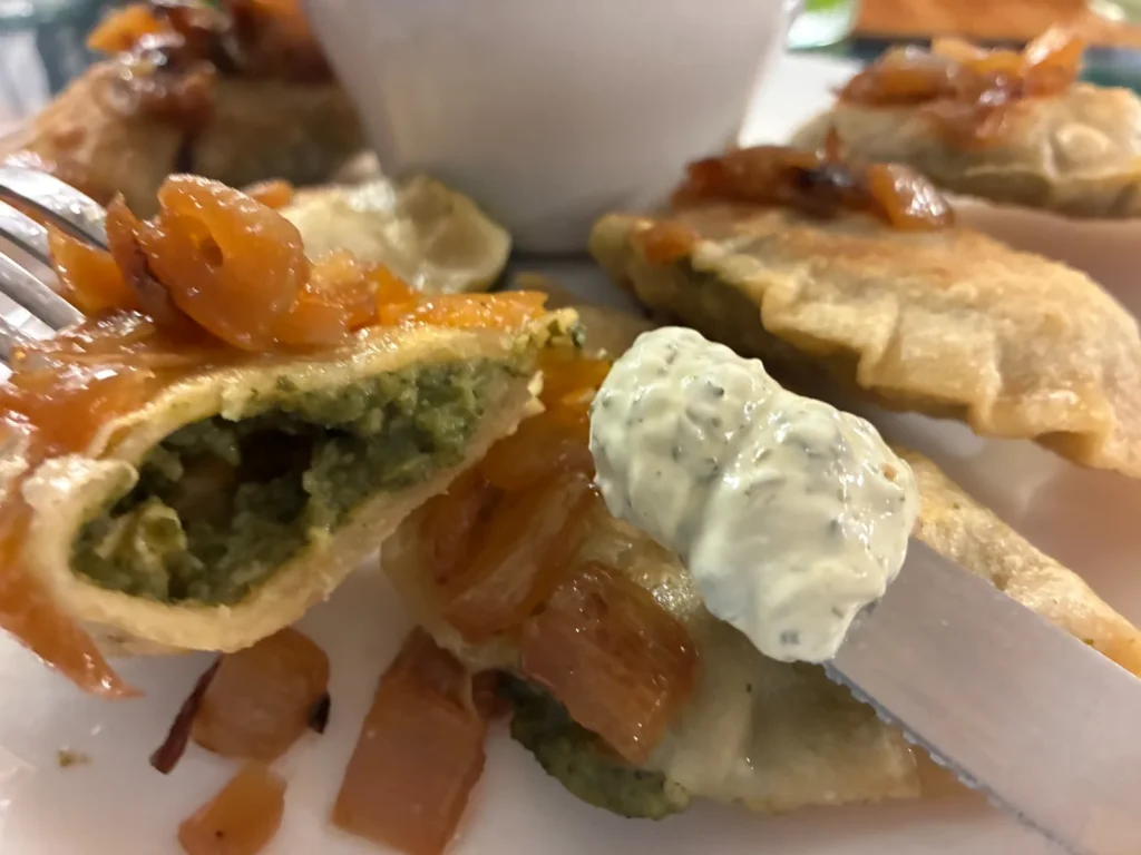 Cut-open spinach and feta cheese pierogi on a fork, served with caramelized onions and creamy artichoke dip at Kat’s Café & Restaurant.