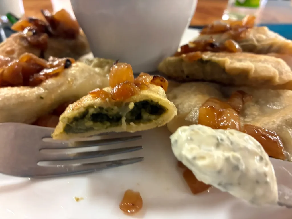 Close-up of a cut-open spinach and feta cheese pierogi showing the green filling, with caramelized onions and artichoke dip at Kat’s Café & Restaurant.