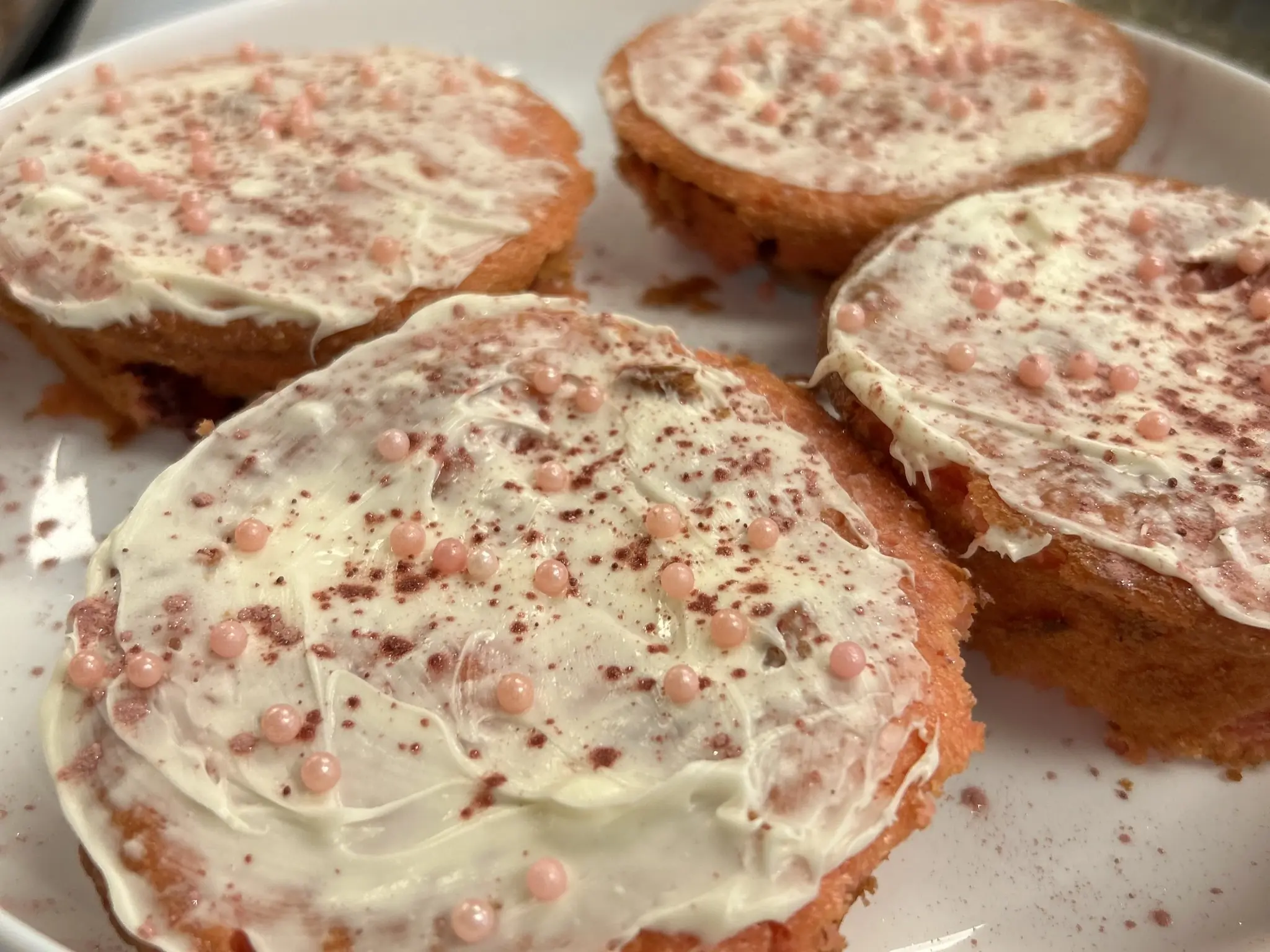 Four strawberry banana mini cakes topped with white frosting, pink sugar pearls, and a light decorative dusting at Kat’s Café & Restaurant.