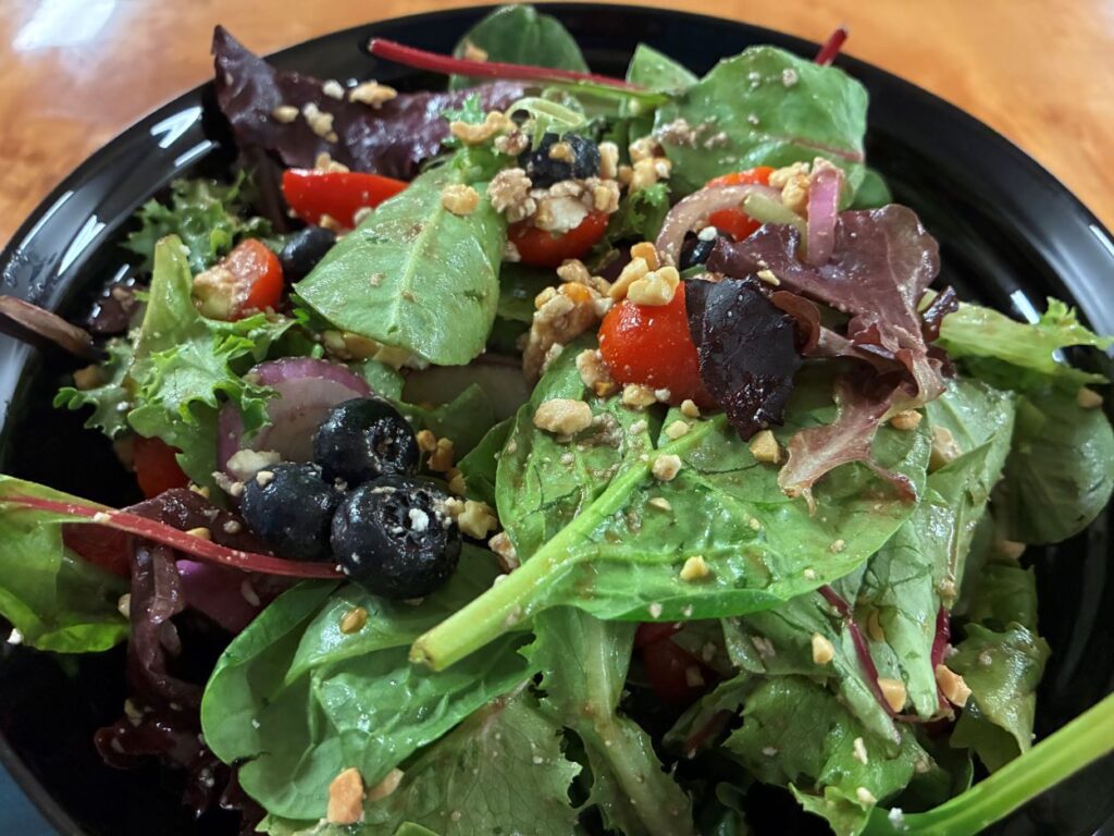 Fresh mixed salad greens with blueberries, raspberries, and chopped peanuts, served in a black bowl.