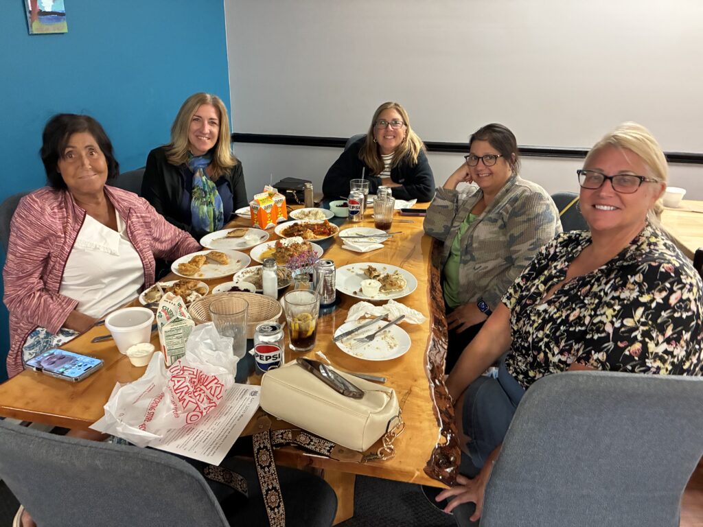 A photo of happy smiling female customers seated around the custom ambrosia live edge table at Kat's with the remnants of their meals on the table.