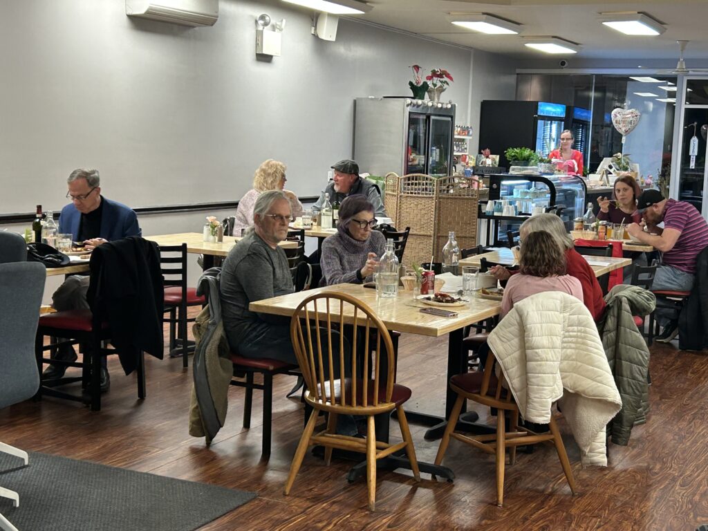 Another photo of happy customers at Kat's in different stages of eating their meals with some tables pulled together for larger groups of customers while others seated by single tables with the front counter area in the background.
